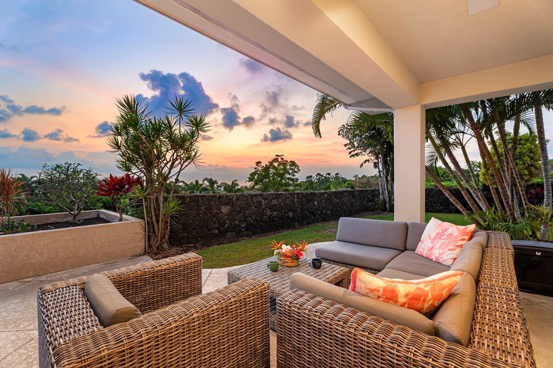 Un patio cubierto con asientos tejidos da a un jardín al atardecer.