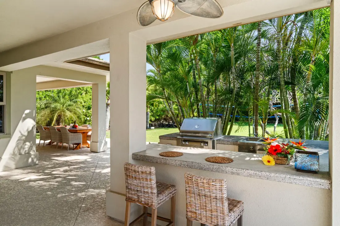 A covered outdoor bar with woven seating overlooks a lush tropical garden.