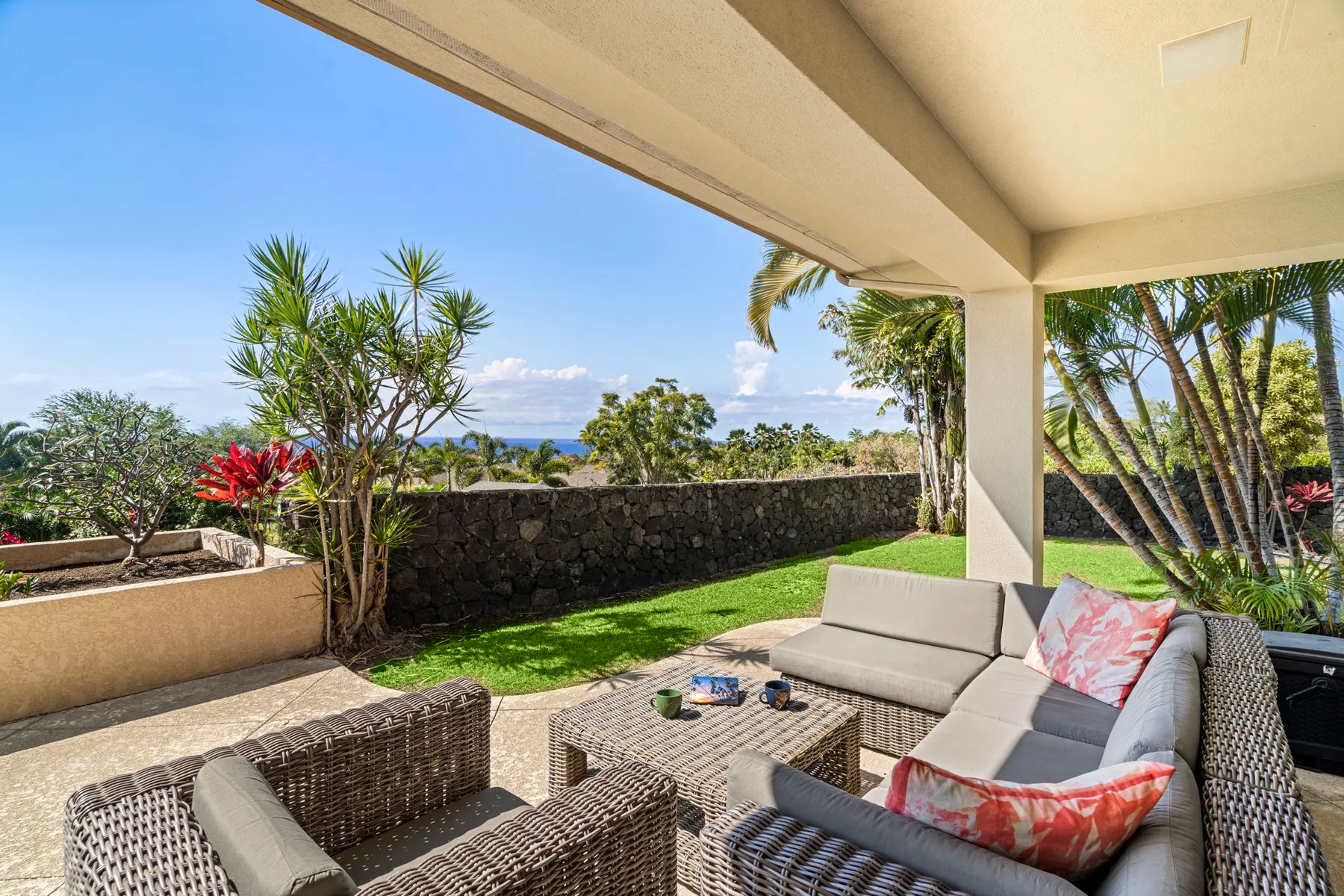 A covered patio with wicker seating overlooks a garden and distant water.