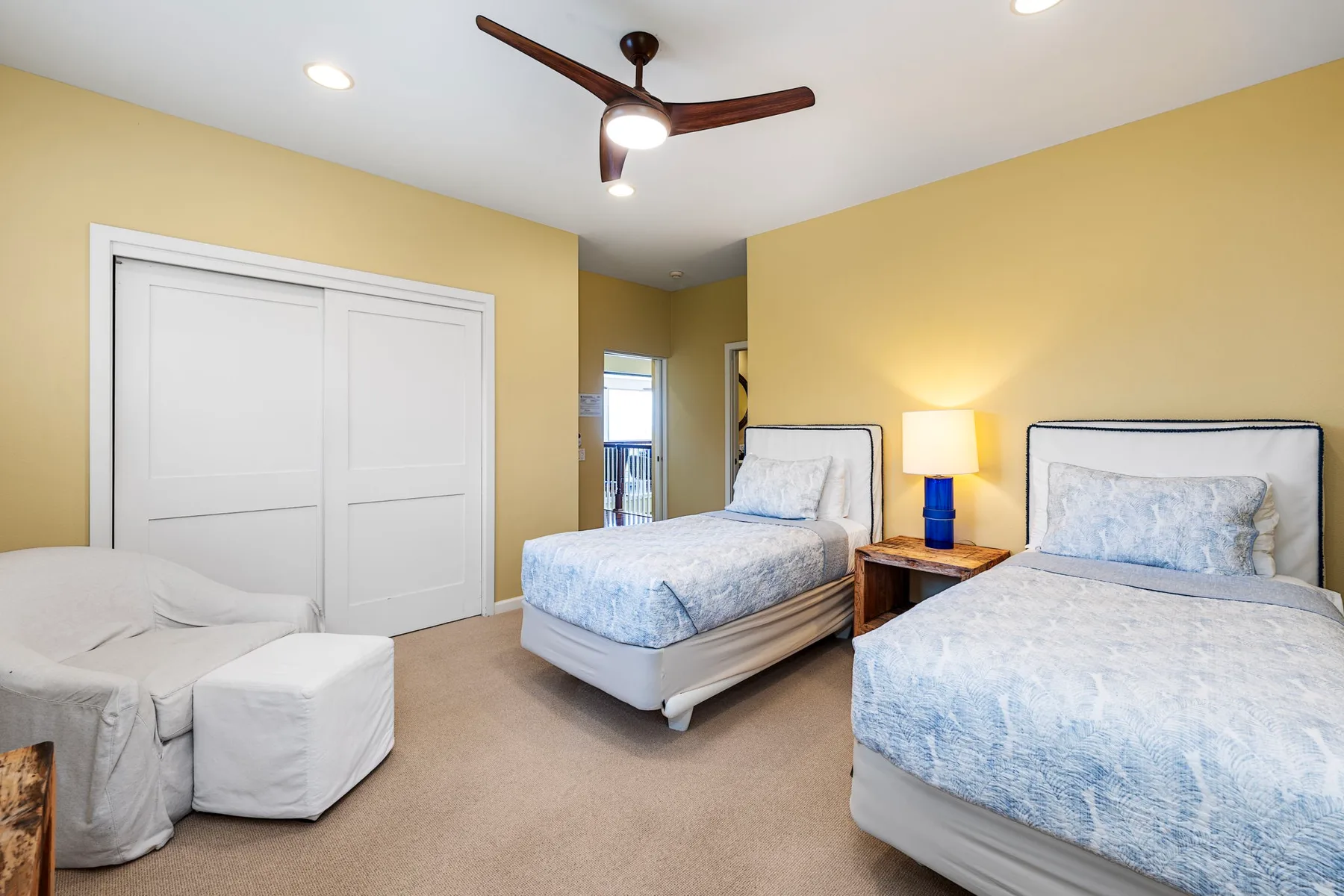 A bedroom with two beds, a ceiling fan, and a small seating area.