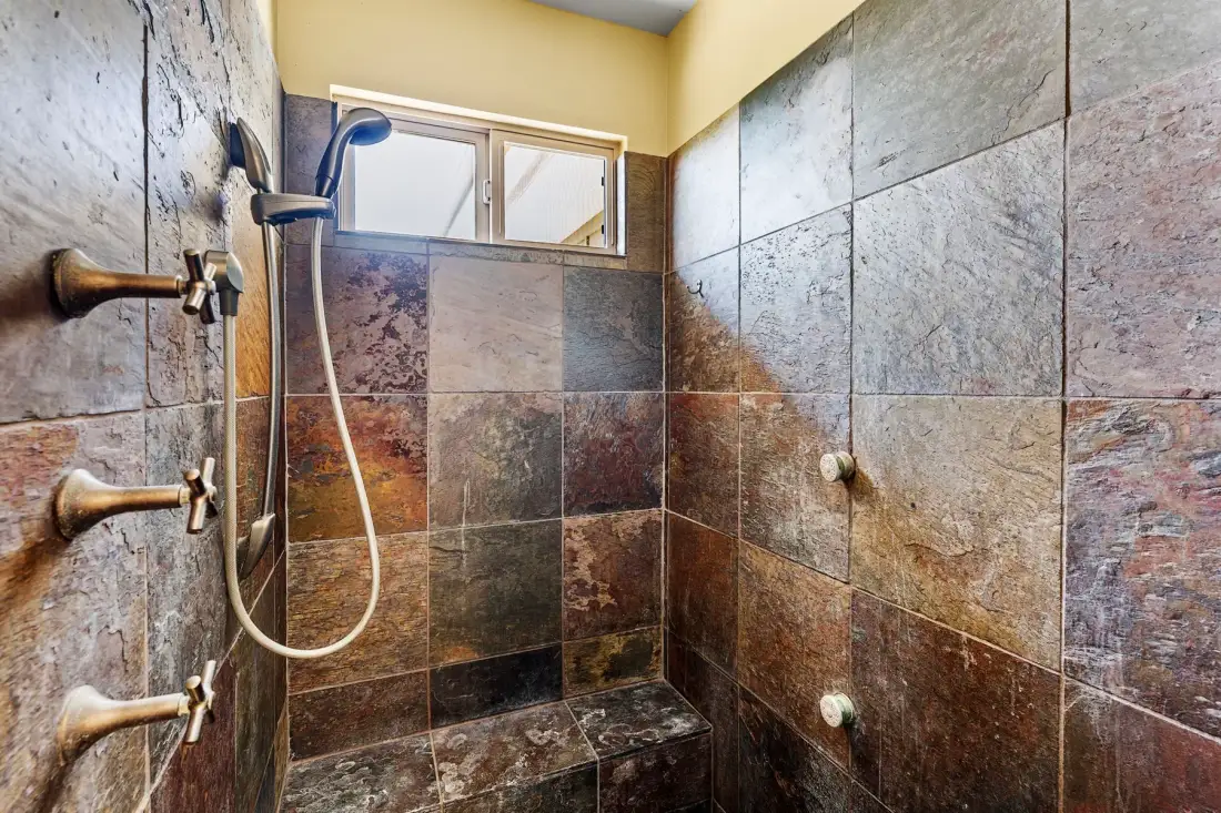 A tiled shower with a handheld showerhead and a small window.