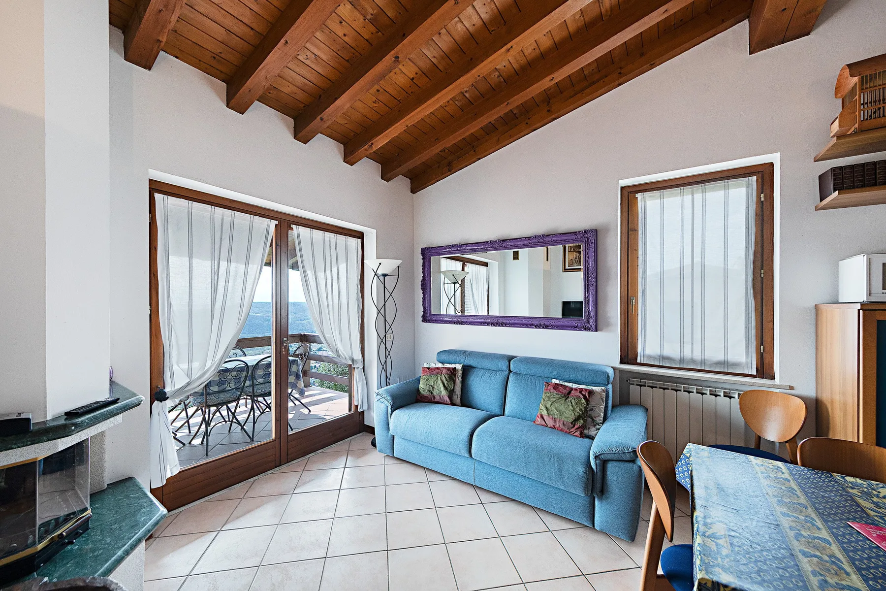 A living room with blue seating, a glass door, and exposed wooden ceiling beams.