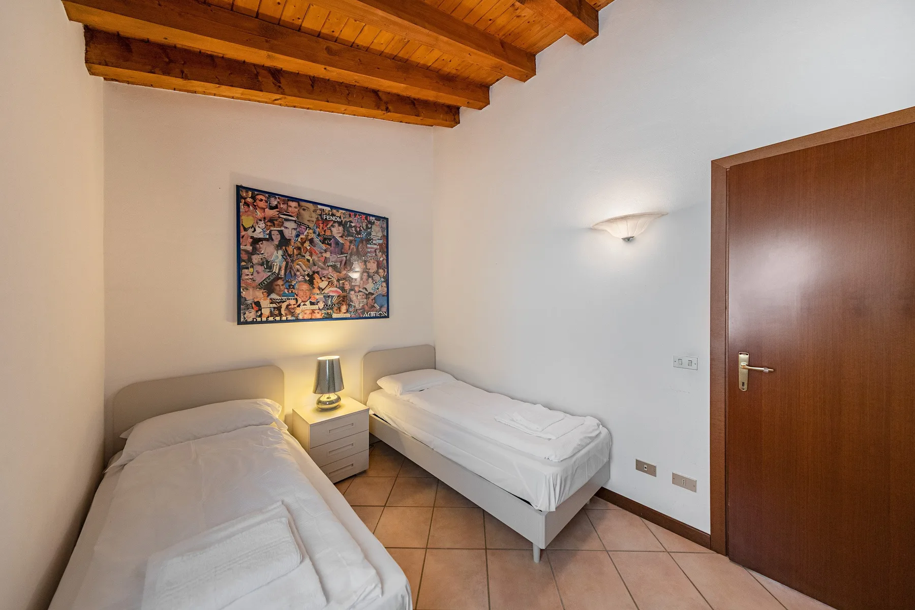 A bedroom with two single beds, a bedside table, and a wooden ceiling.