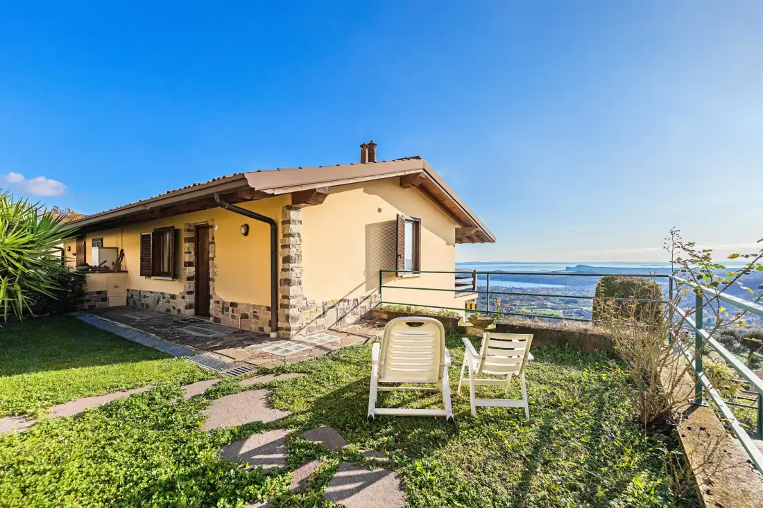 A small house with a grassy yard and outdoor seating overlooks the water.