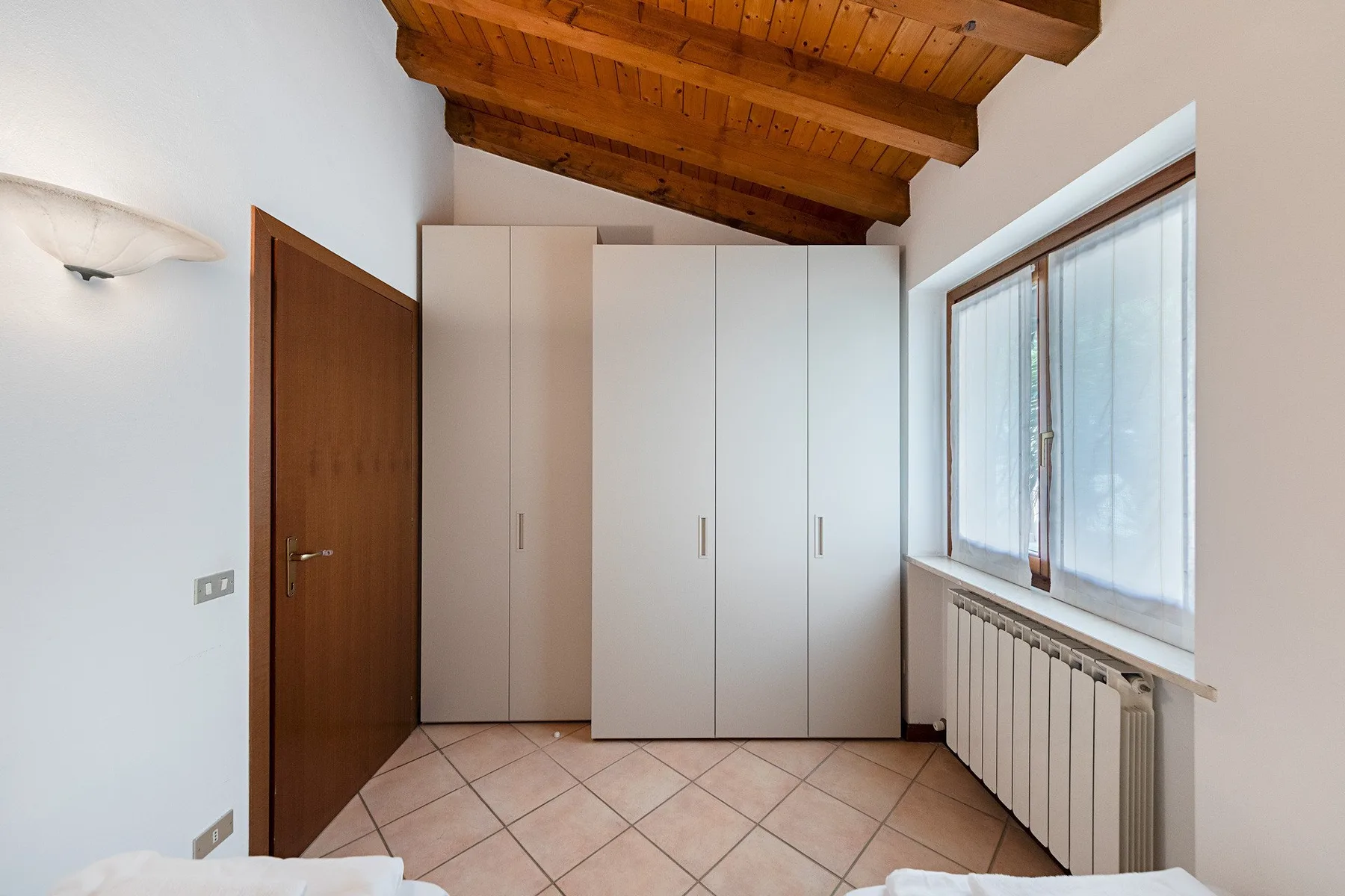 A bedroom with a large built-in wardrobe and a window beside the radiator.