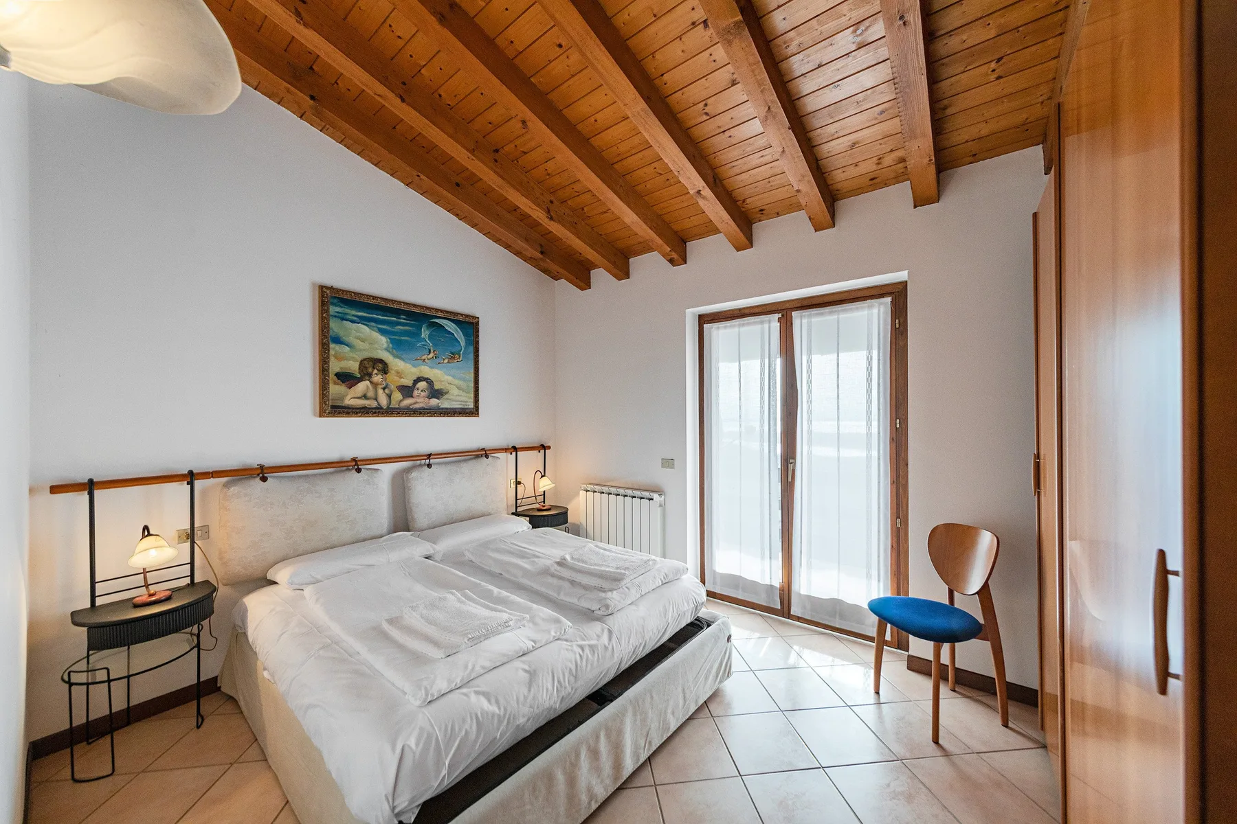 Bedroom with a large bed beneath a wooden-beamed ceiling.
