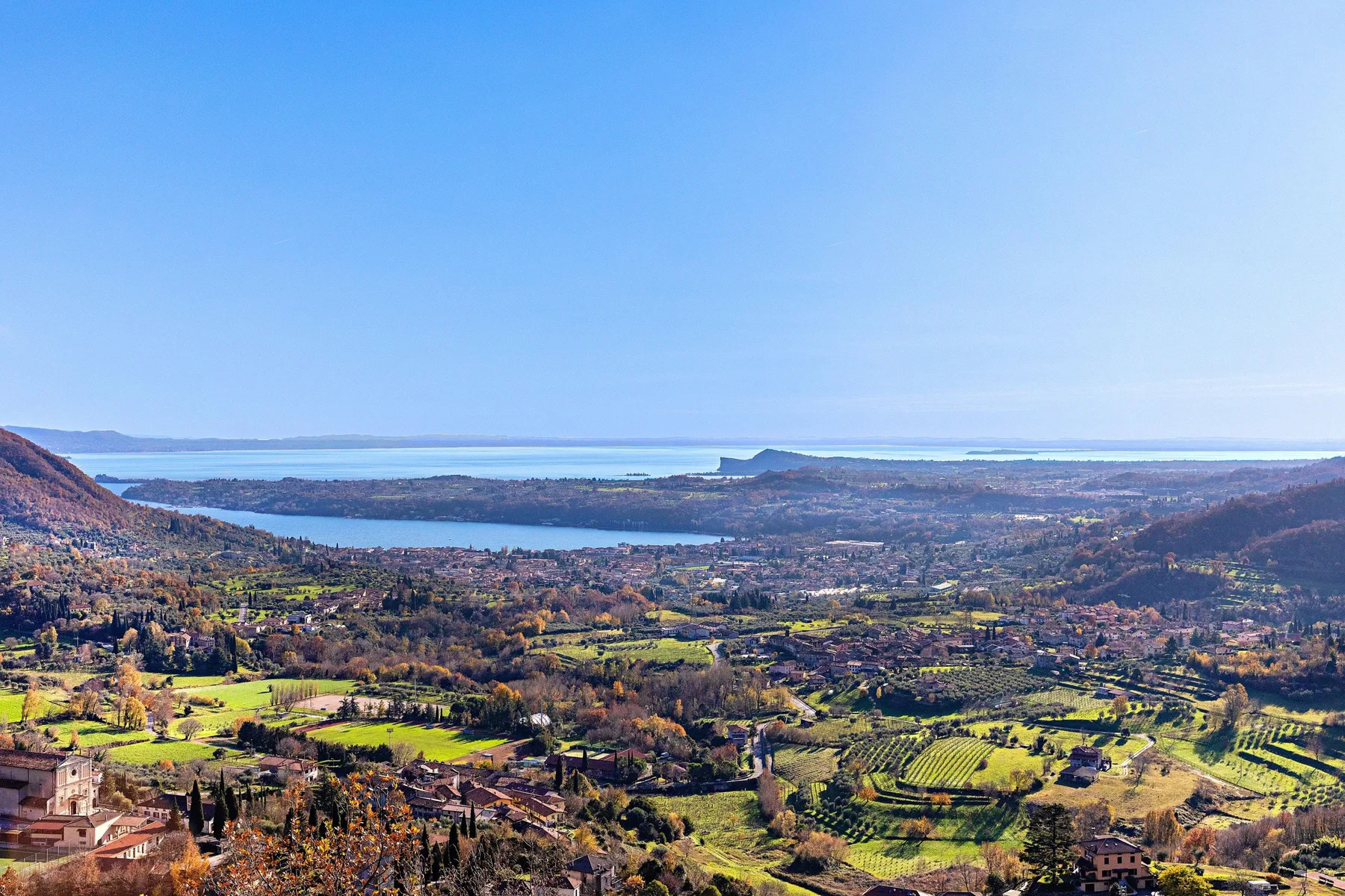 A broad landscape view shows fields and hills surrounding a lake beneath a clear sky.