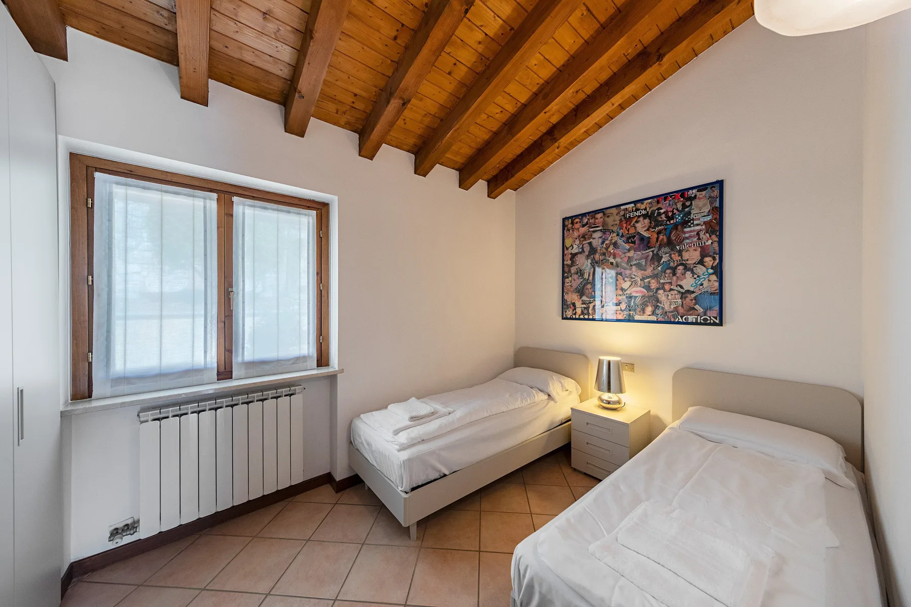 A bedroom with two single beds, a bedside table, and a sloped wooden ceiling.