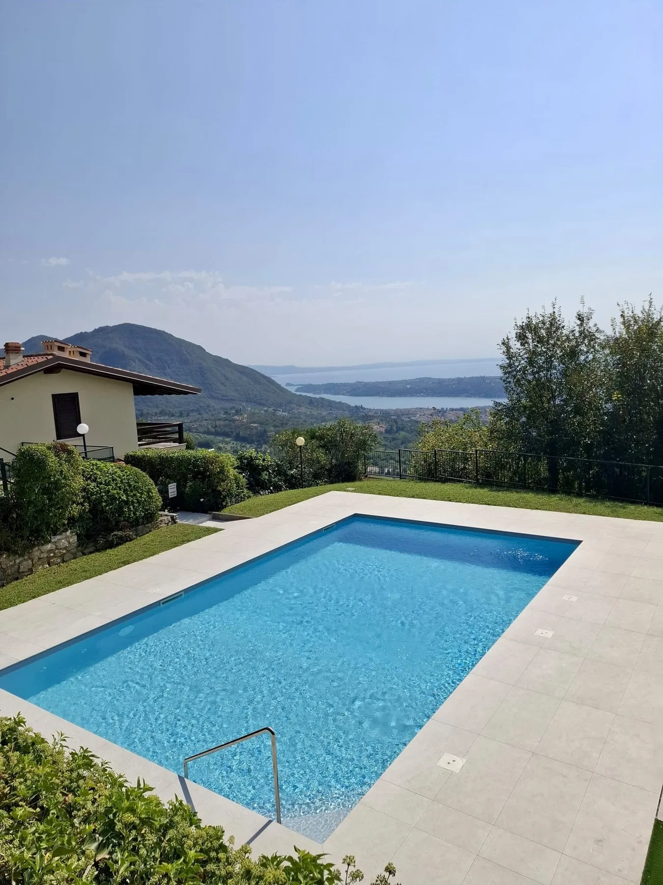 A swimming pool and paved deck overlook a distant lake and hills.