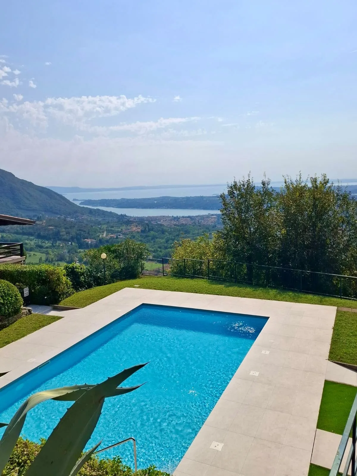 An outdoor swimming pool overlooks green hills and a distant body of water.