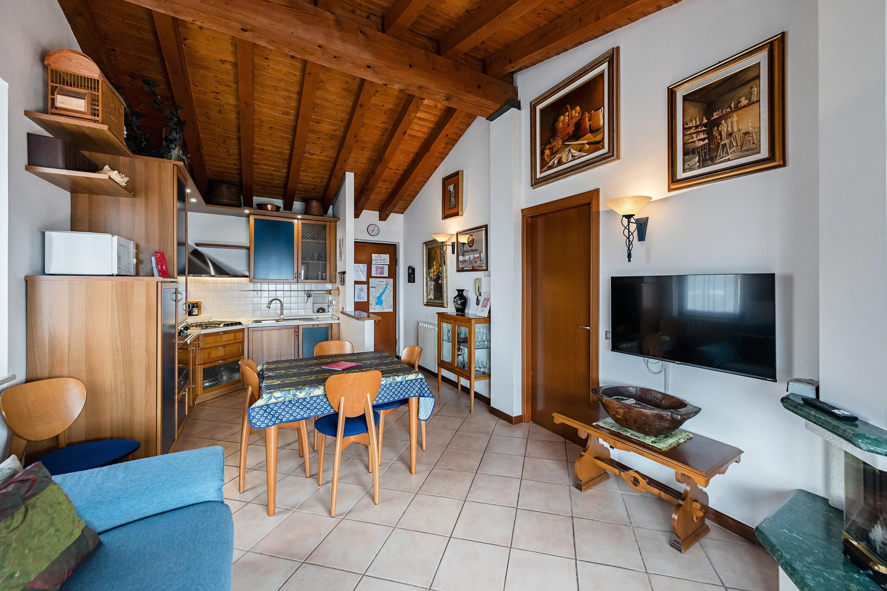 A combined kitchen and dining area with a table beneath a sloped wooden ceiling.
