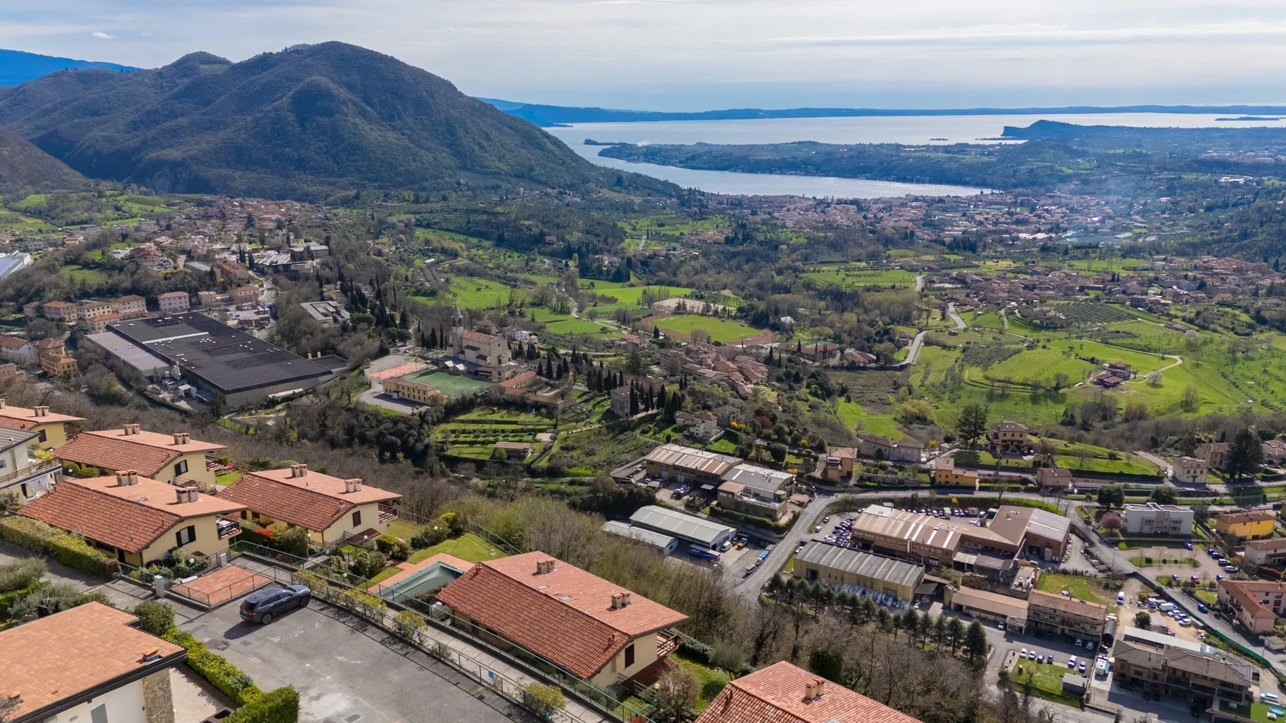 An aerial view of a lakeside town, with green fields and hills in the distance.