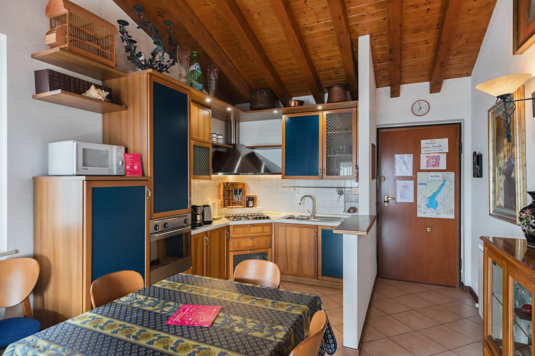 A dining area beside a compact kitchen, with a patterned tablecloth and wooden cabinetry.