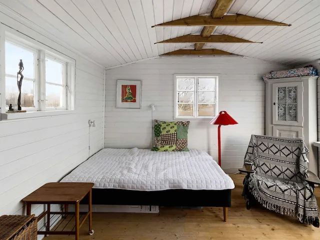 A bedroom with a bed, a red floor lamp, and a patterned chair.