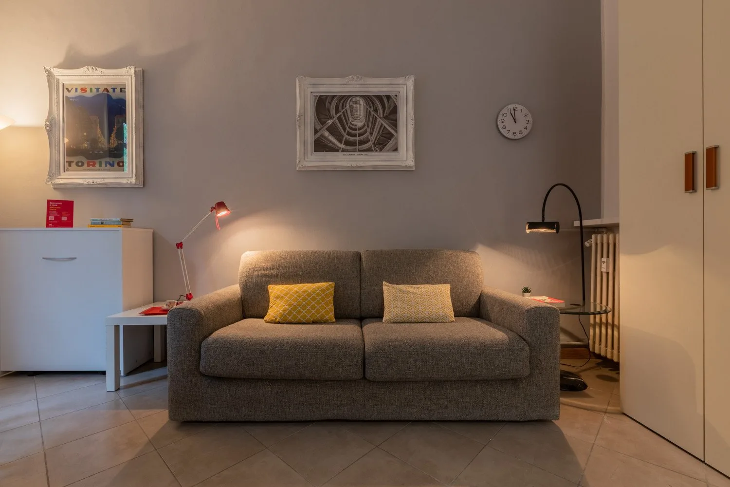 Una sala de estar con un sofá gris, cuadros en la pared y luz cálida.