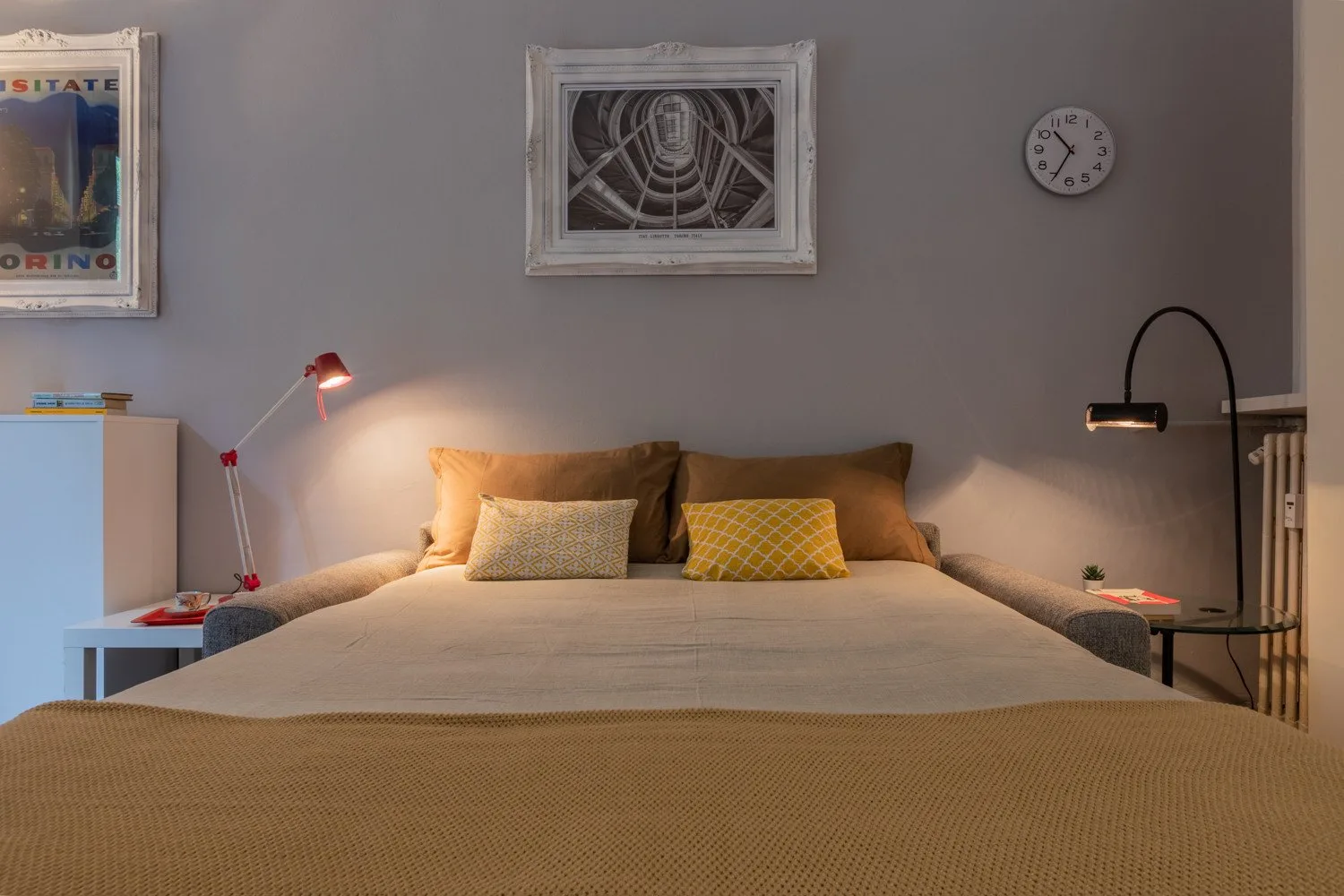 Un dormitorio con una cama tendida, lámparas de noche y cuadros en la pared.