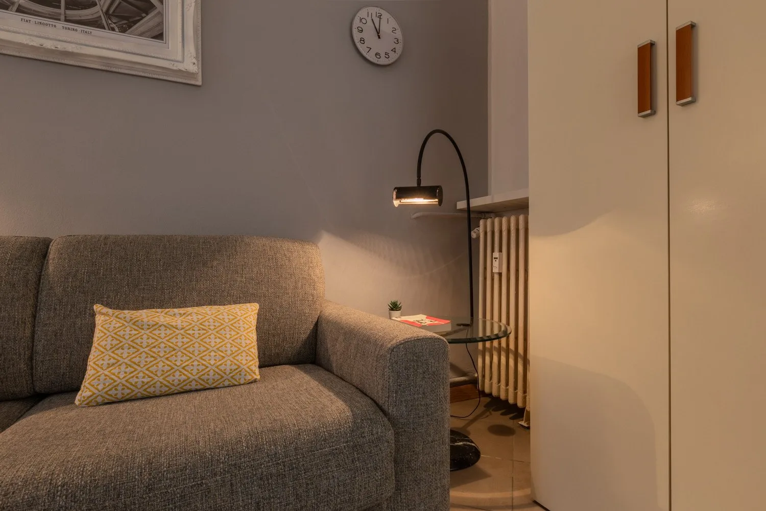 Una sala de estar con un sofá gris y una lámpara de pie junto a un armario.