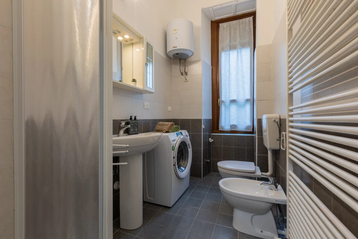 Un baño estrecho con lavabo, lavadora, inodoro y ventana.
