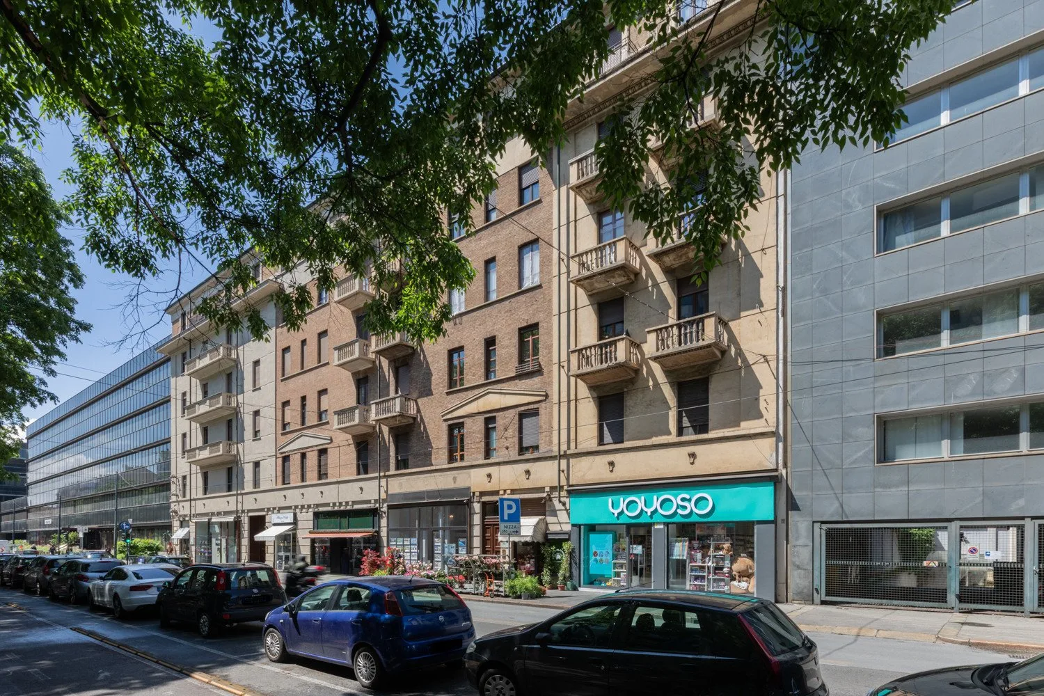 Una calle urbana con edificios de varias plantas, comercios y coches estacionados.