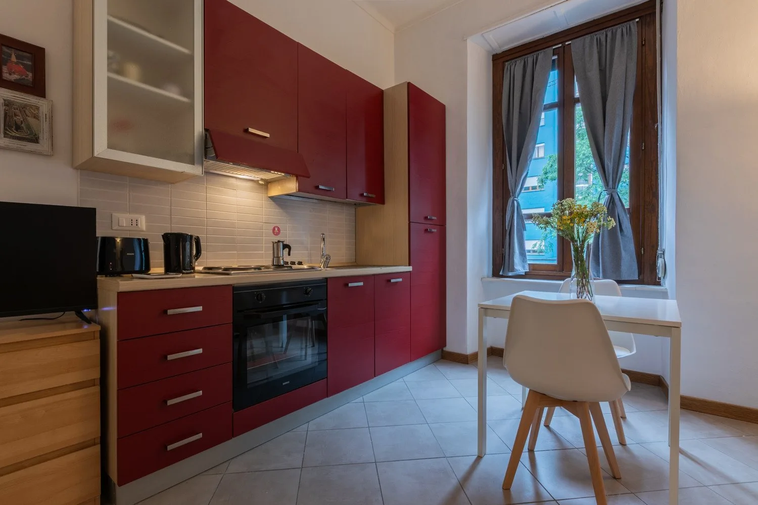 Una cocina compacta con gabinetes rojos y una pequeña mesa junto a la ventana.