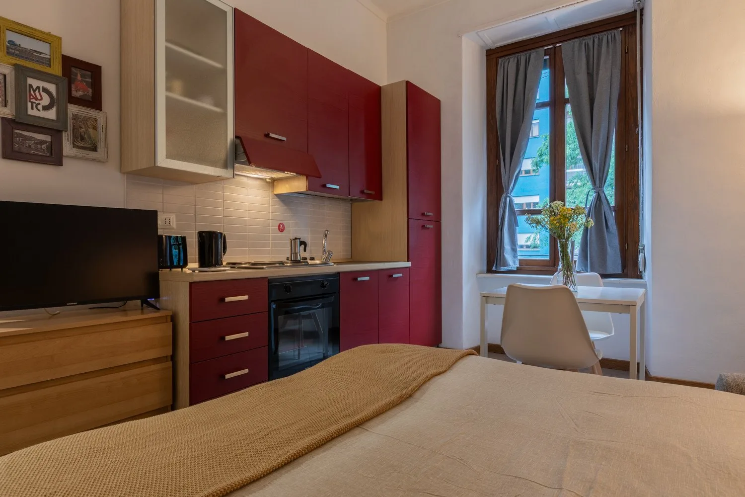 Dormitorio con una pequeña cocina y una ventana con vistas a edificios cercanos.
