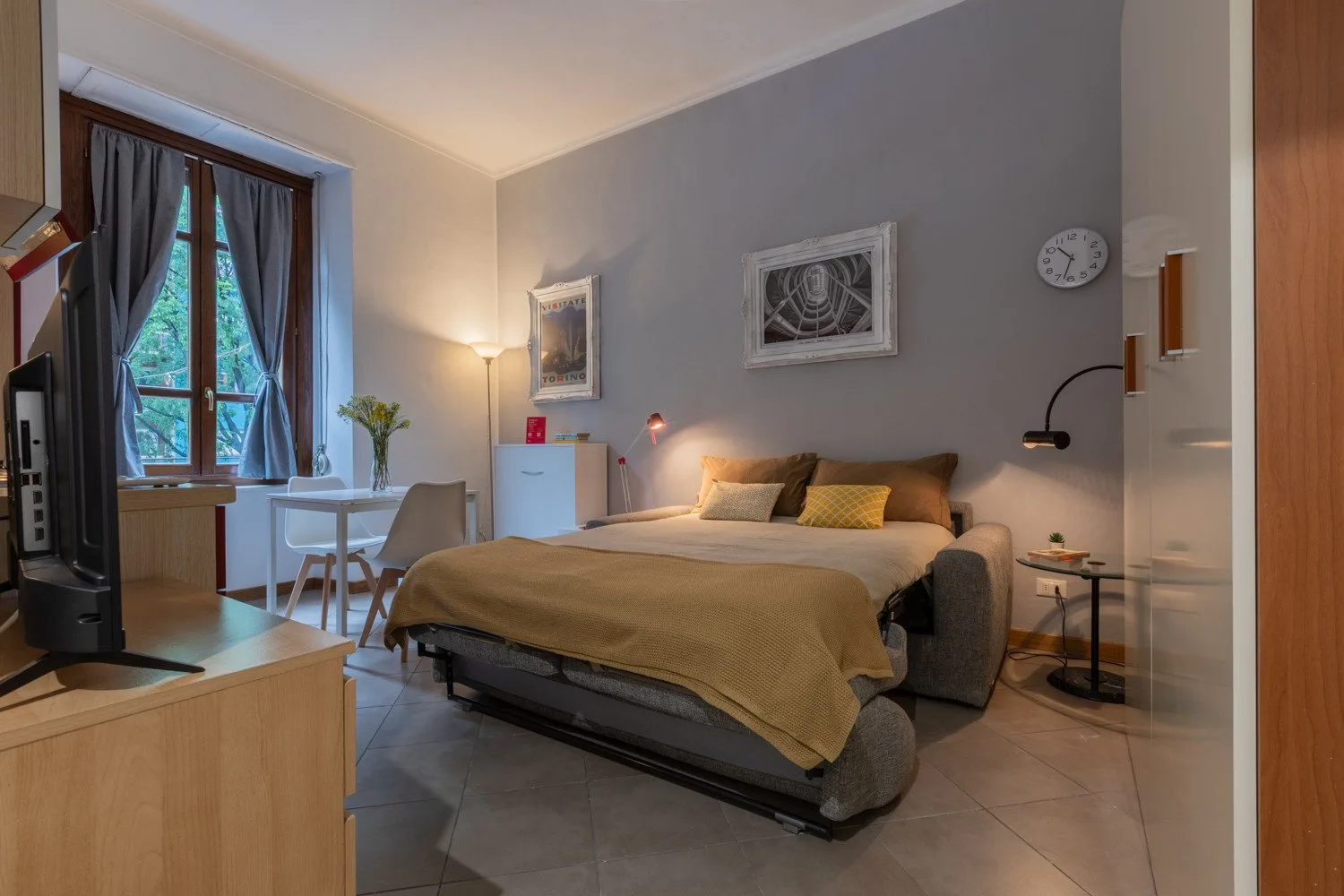 Un dormitorio con una cama, asientos y una pequeña mesa junto a la ventana.