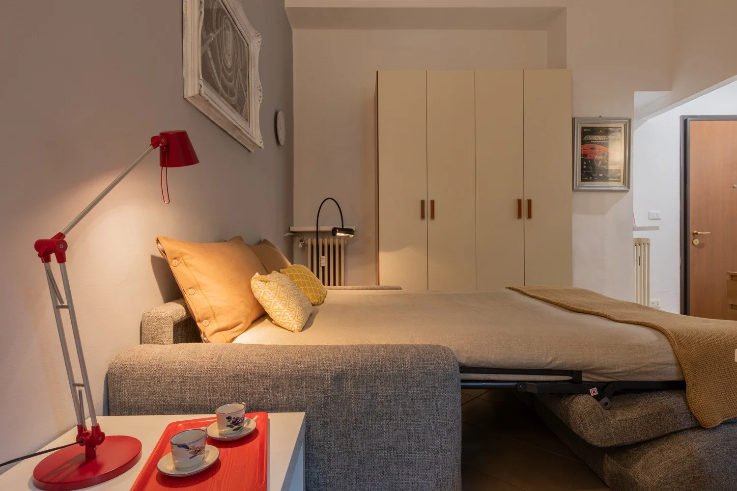 Un dormitorio con una cama, asientos grises y un armario alto.