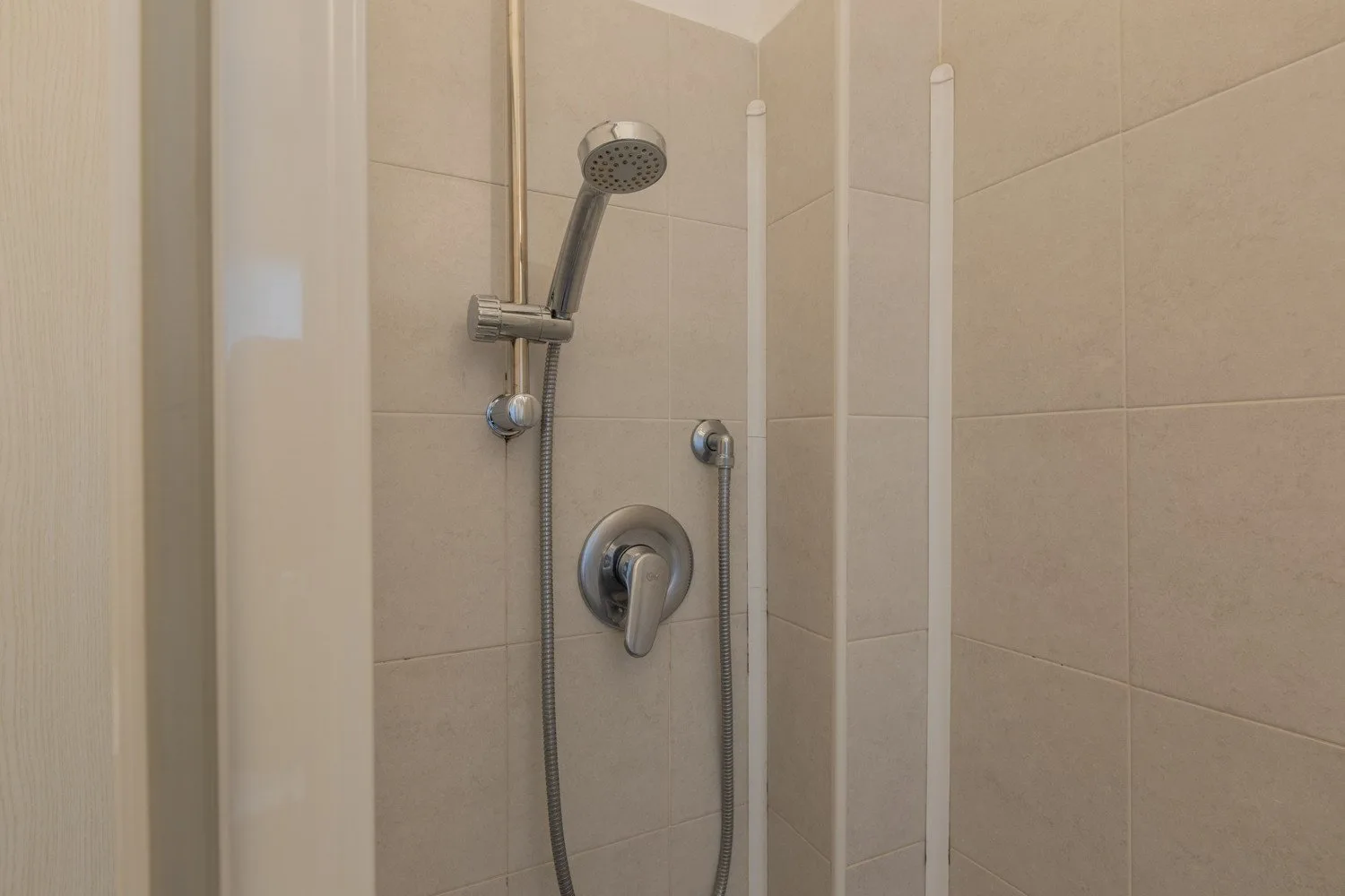 Una ducha con azulejos, alcachofa de mano y controles montados en la pared.