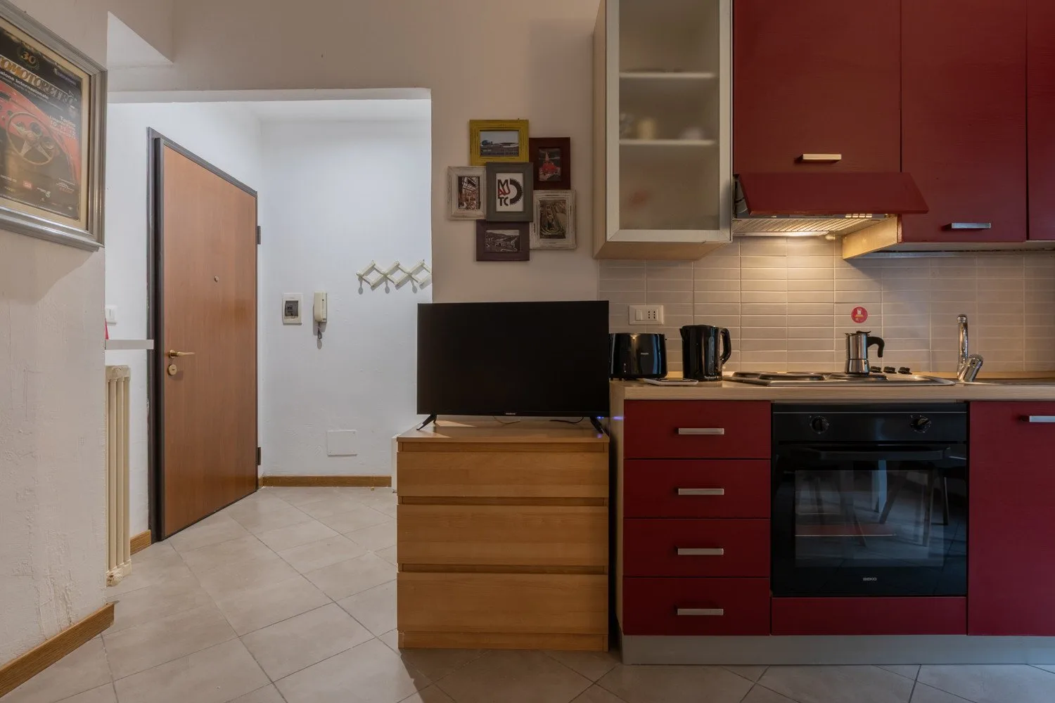 Una cocina compacta con gabinetes rojos, una estufa y un televisor sobre una cómoda de madera.