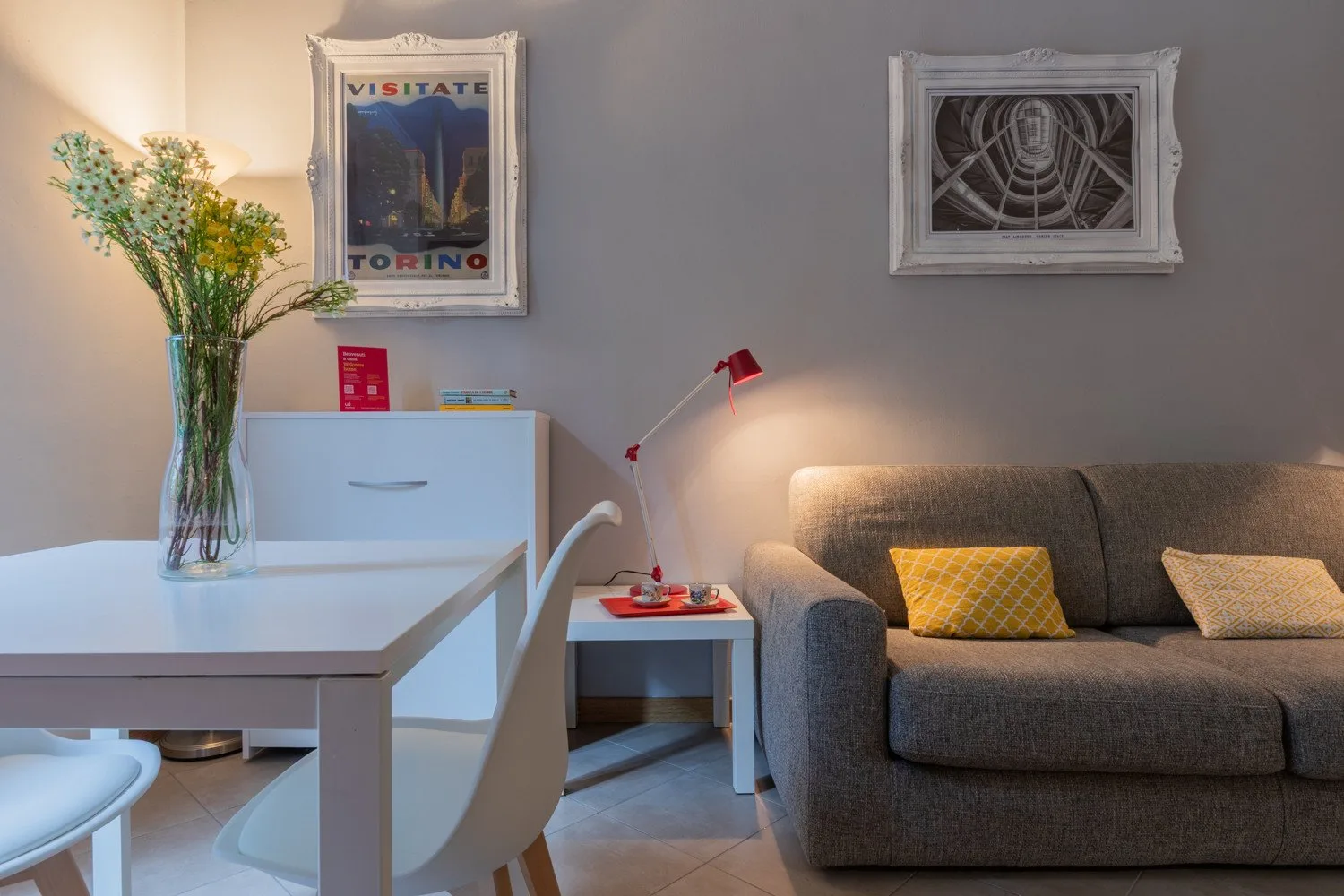 Una sala de estar con un sofá gris, una mesa blanca y cuadros enmarcados.