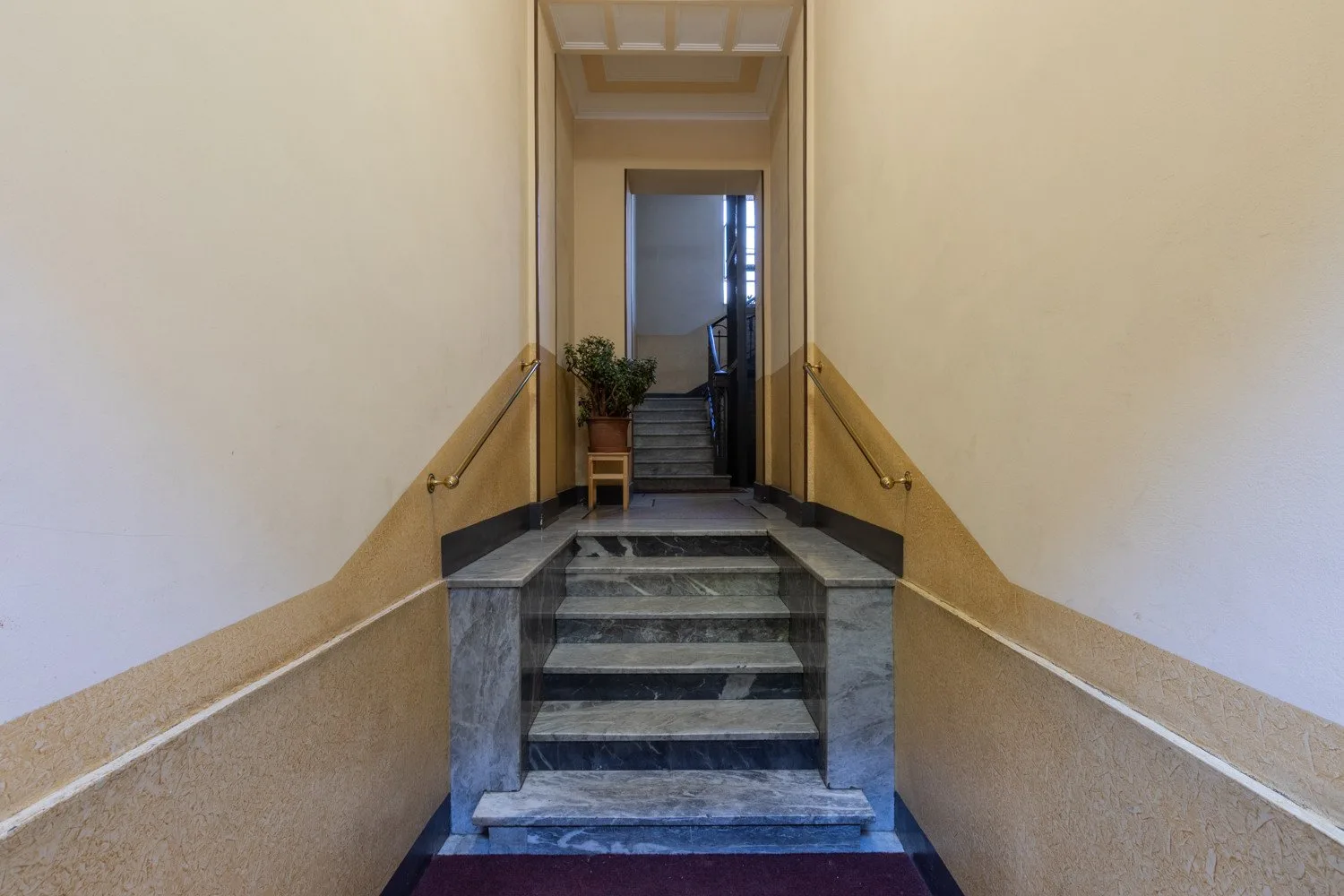 Una estrecha escalera interior sube entre paredes claras con pasamanos.