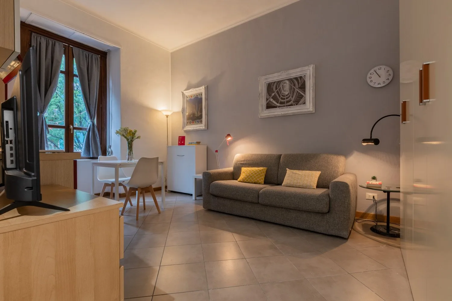 Una sala de estar con un sofá gris y una mesa de comedor junto a la ventana.