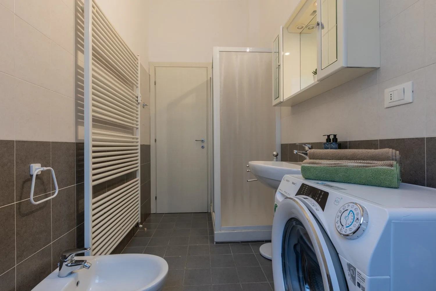 Un baño alicatado con ducha, lavadora y radiador toallero de pared.