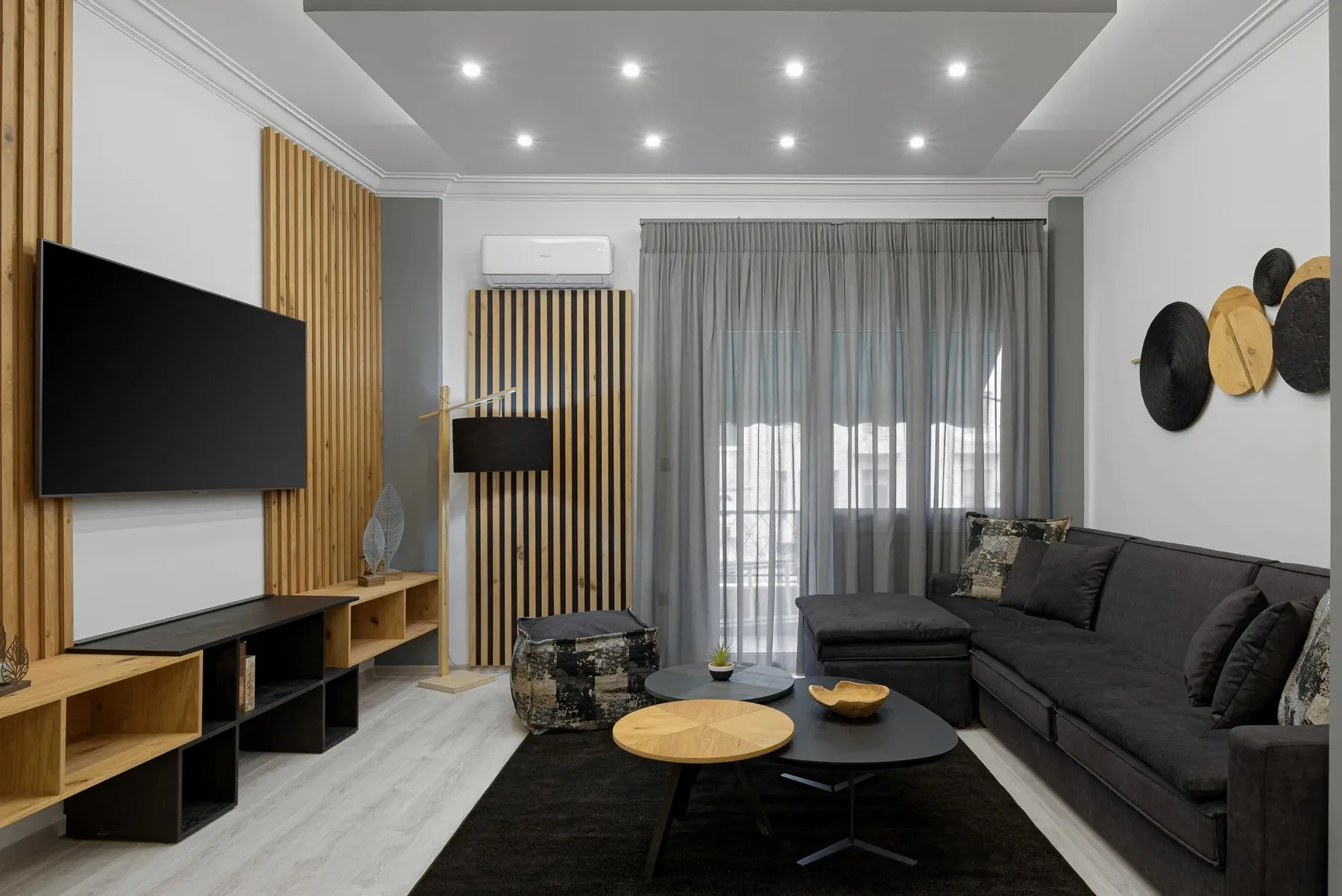 A modern living room with dark seating, a television, and sheer curtains.