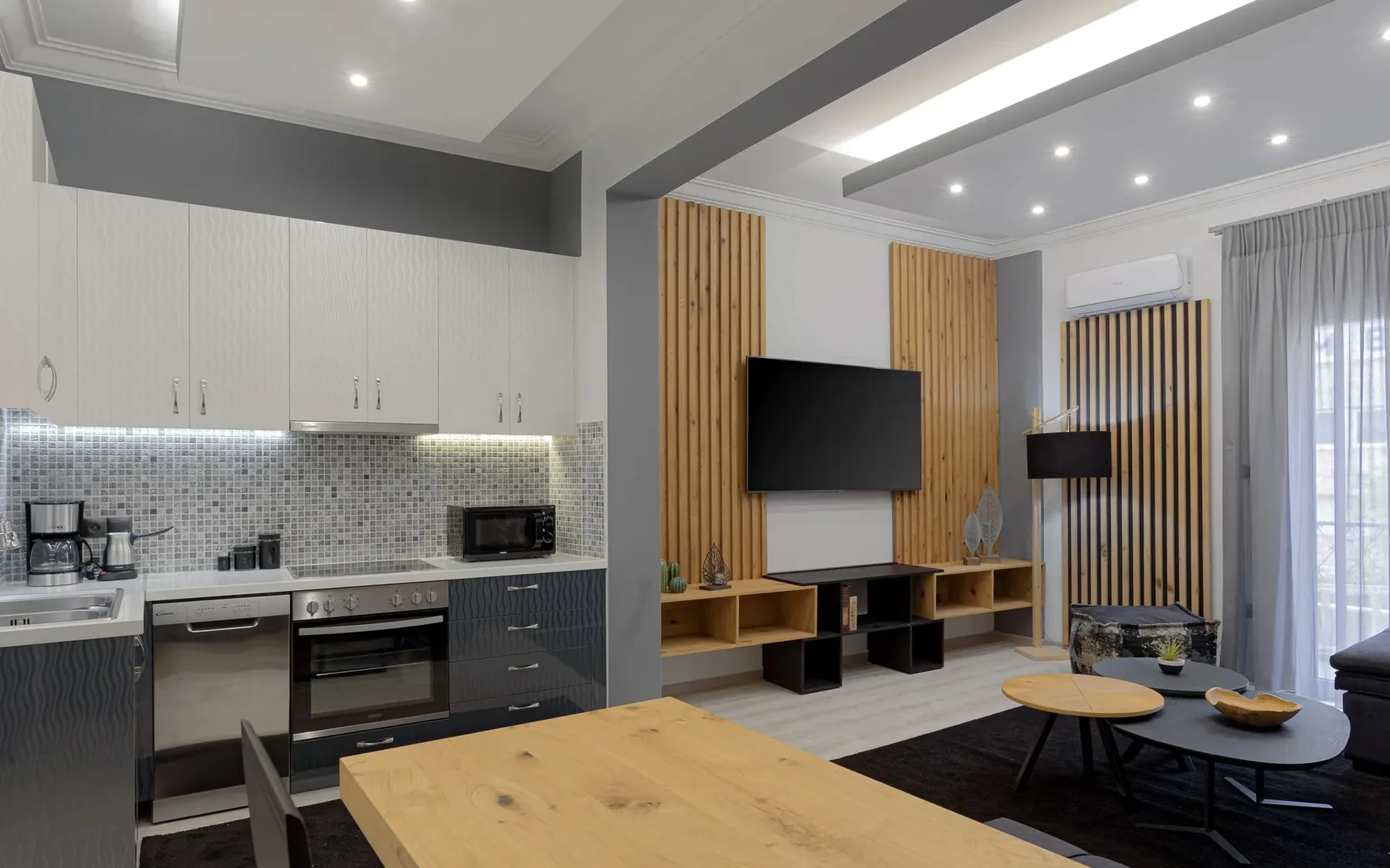 A modern living room with a television, seating, and a dining table.