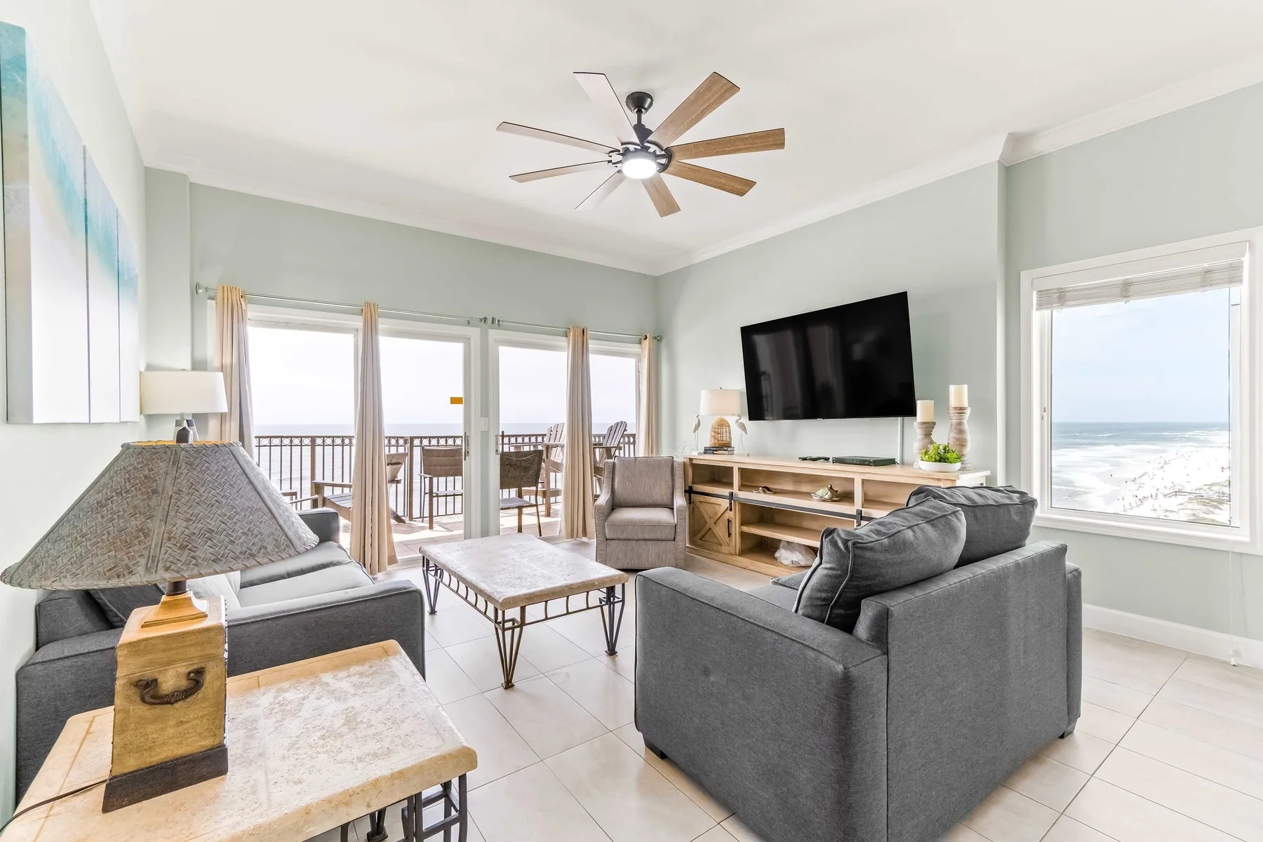 A living room with gray seating, a television, and windows overlooking the ocean.