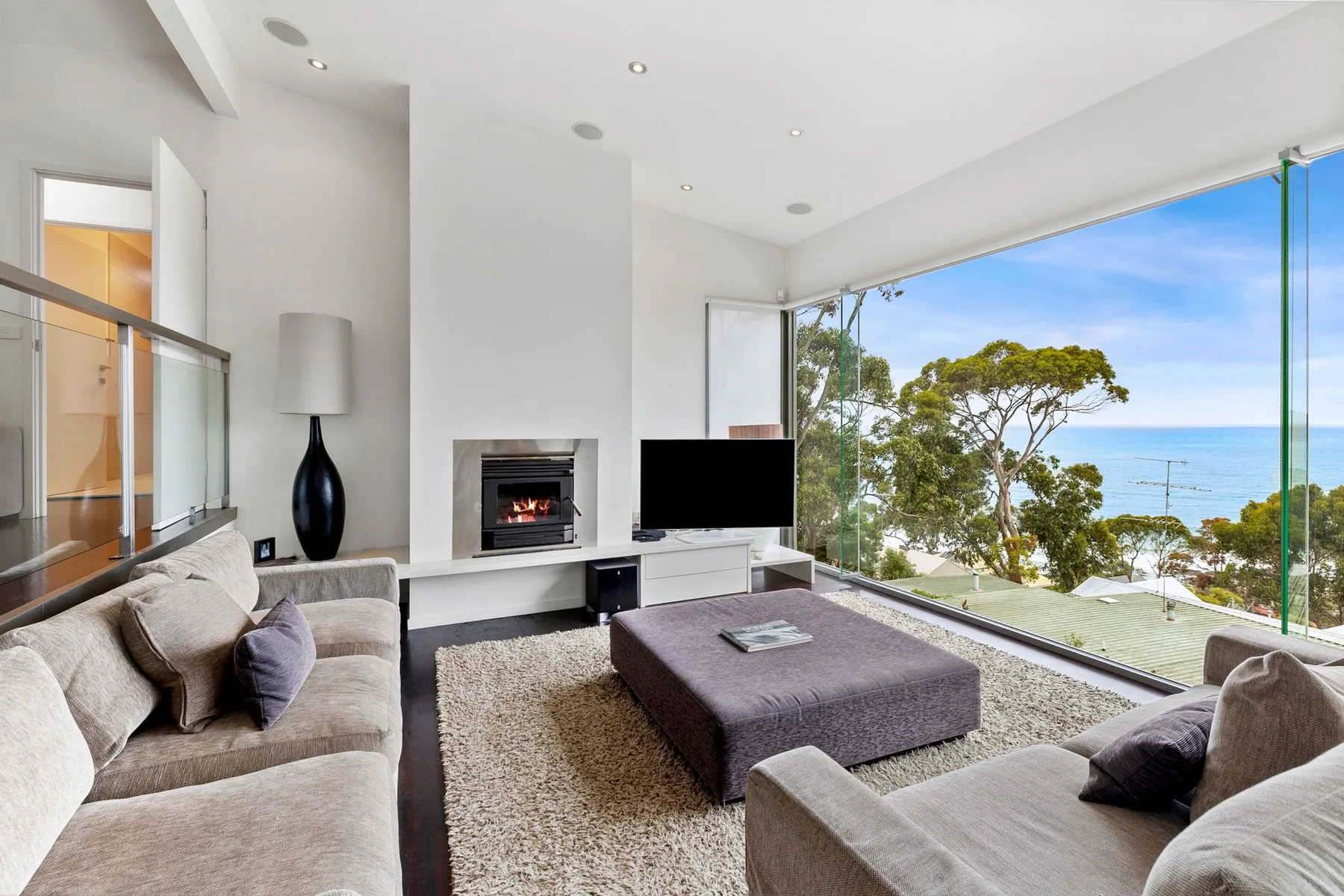 Una luminosa sala de estar con asientos, un televisor y amplias ventanas con vistas al mar.