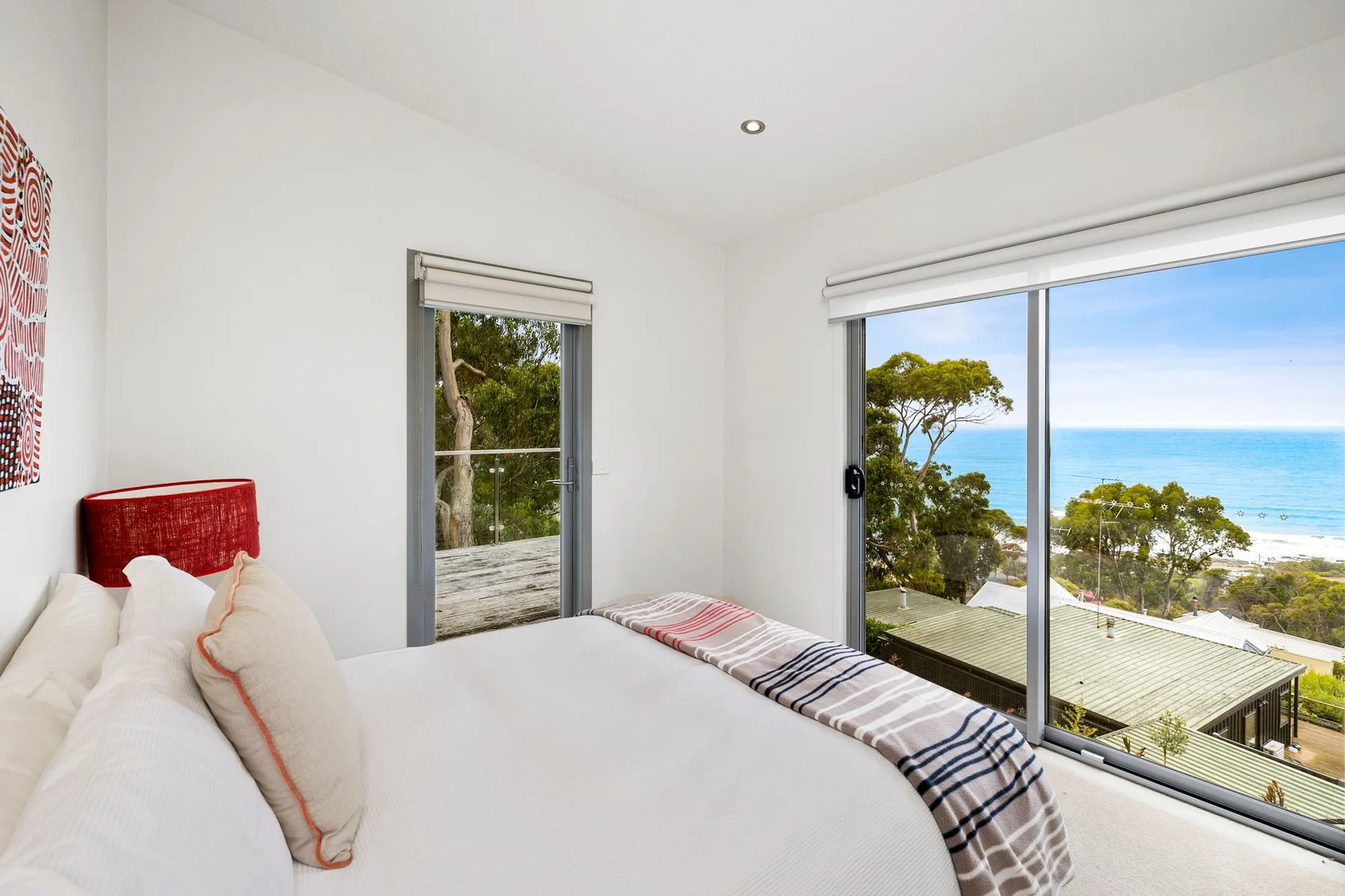 Un dormitorio luminoso con una cama junto a grandes ventanas con vistas al mar.