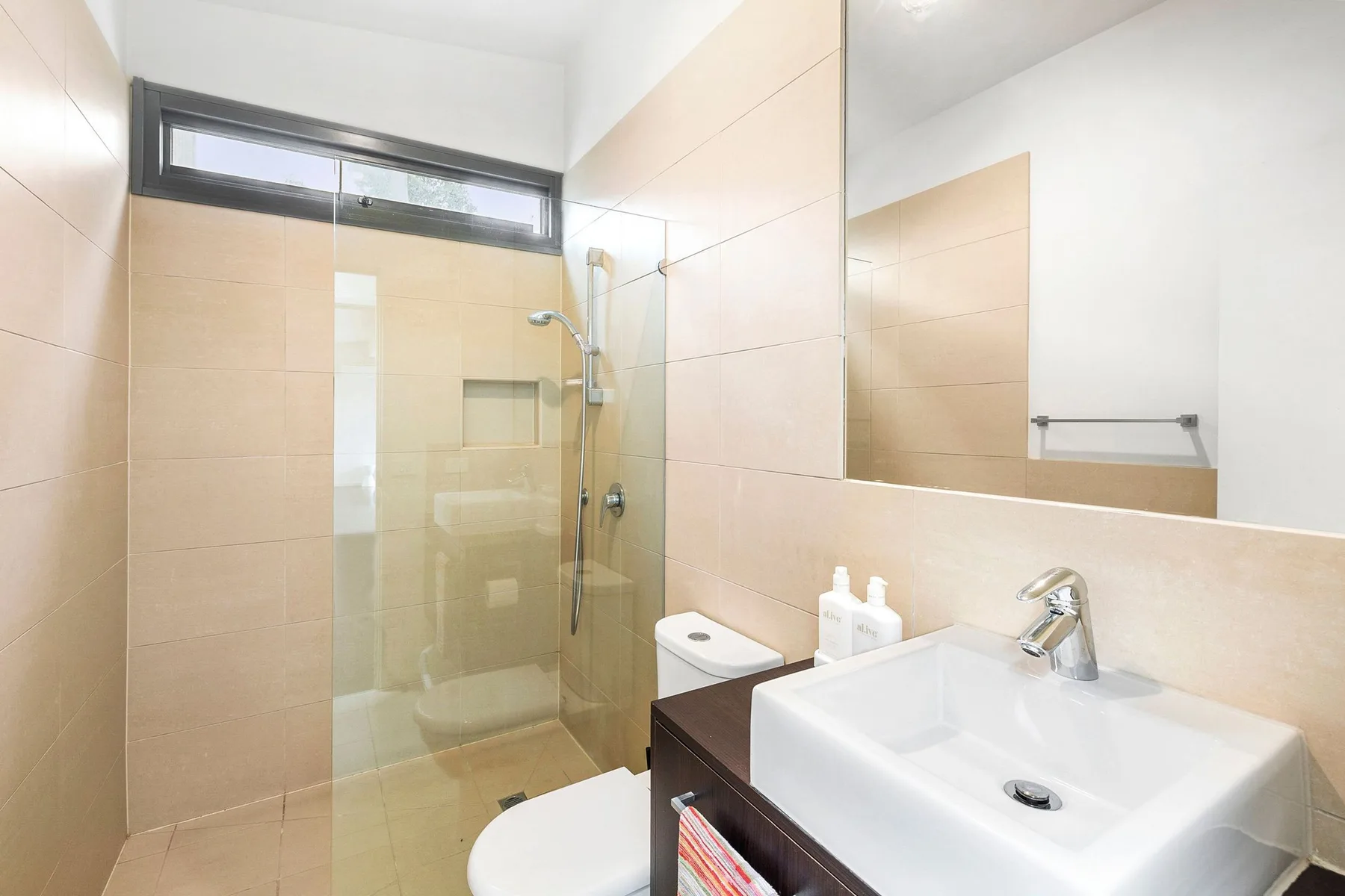 Un baño alicatado con ducha de vidrio, lavabo y espejo.