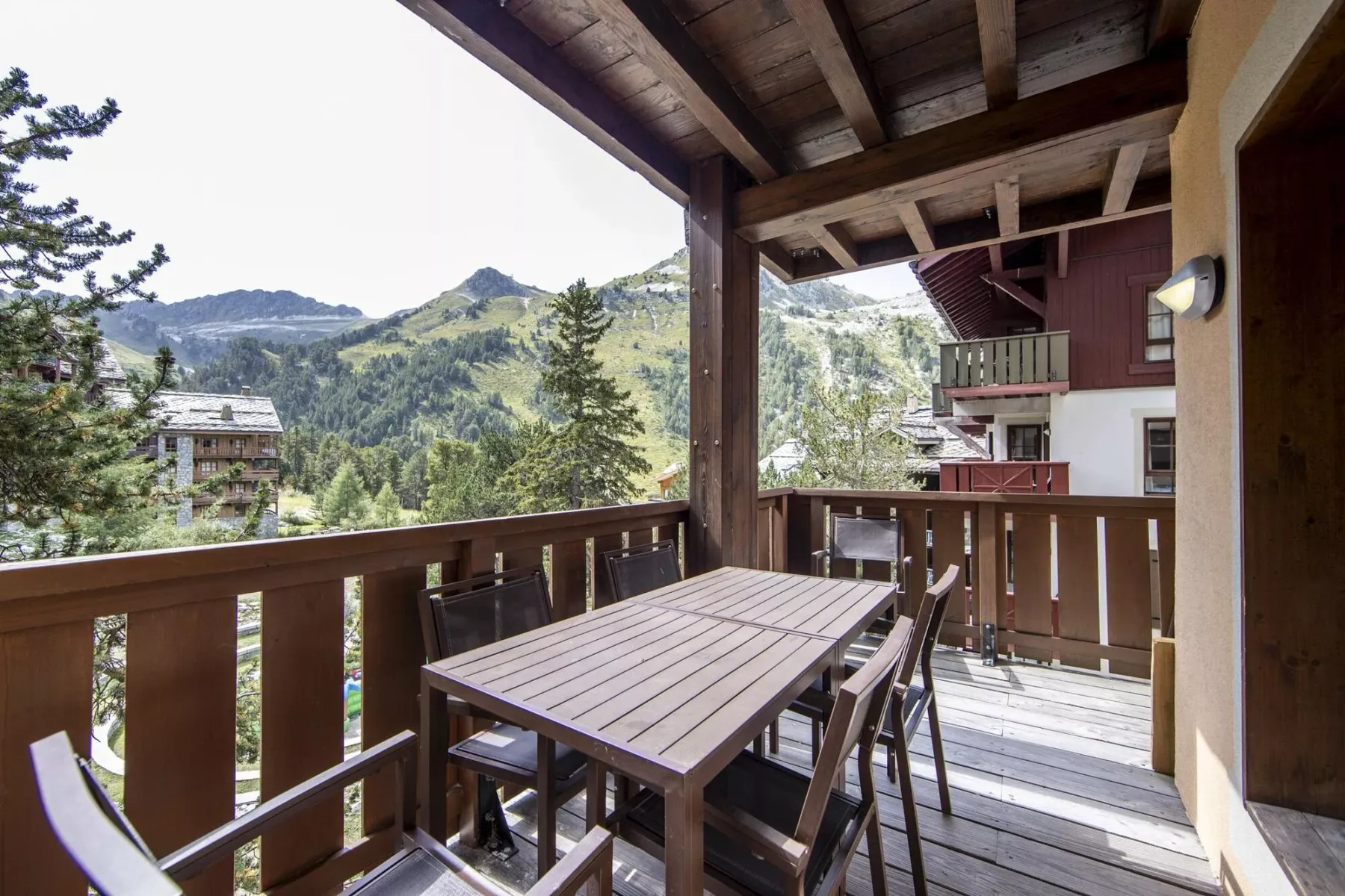 A covered wooden balcony has a dining table and mountain views.