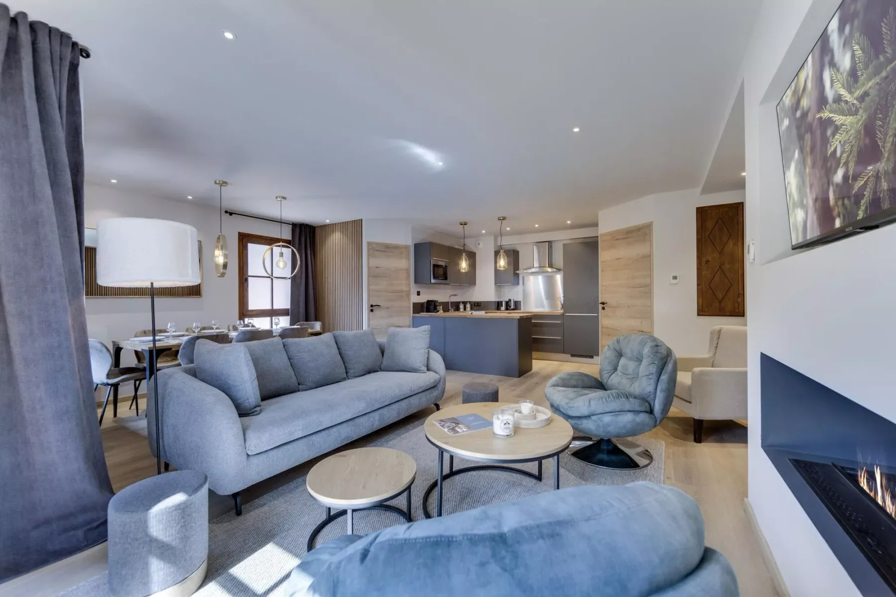 A modern living room opens onto a kitchen, with blue seating and a fireplace.