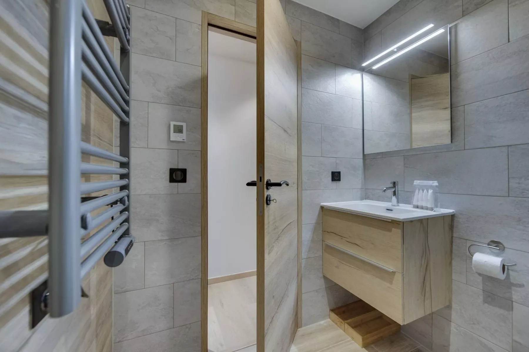 A tiled bathroom with a vanity, mirror, and wall-mounted towel warmer.