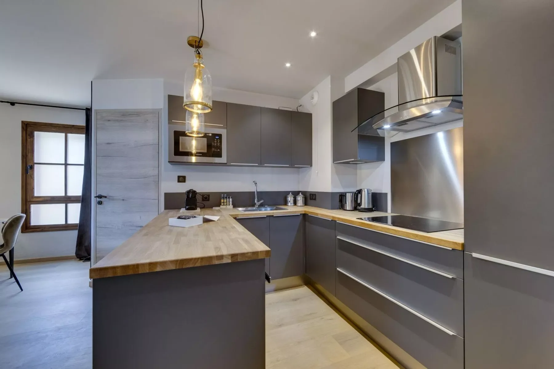 A modern kitchen with gray cabinets, a wooden island, and stainless steel appliances.