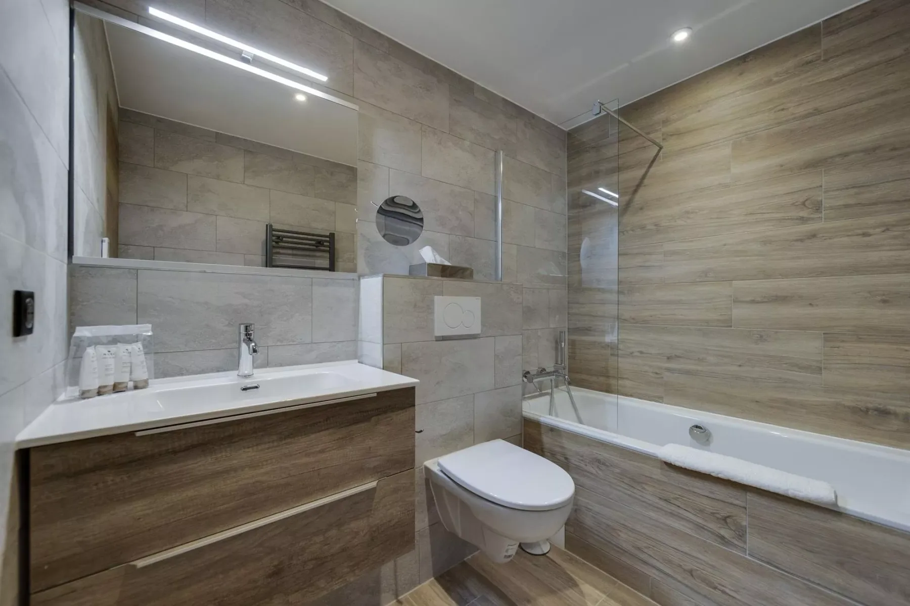 A modern bathroom with a vanity, wall-mounted toilet, and bathtub.