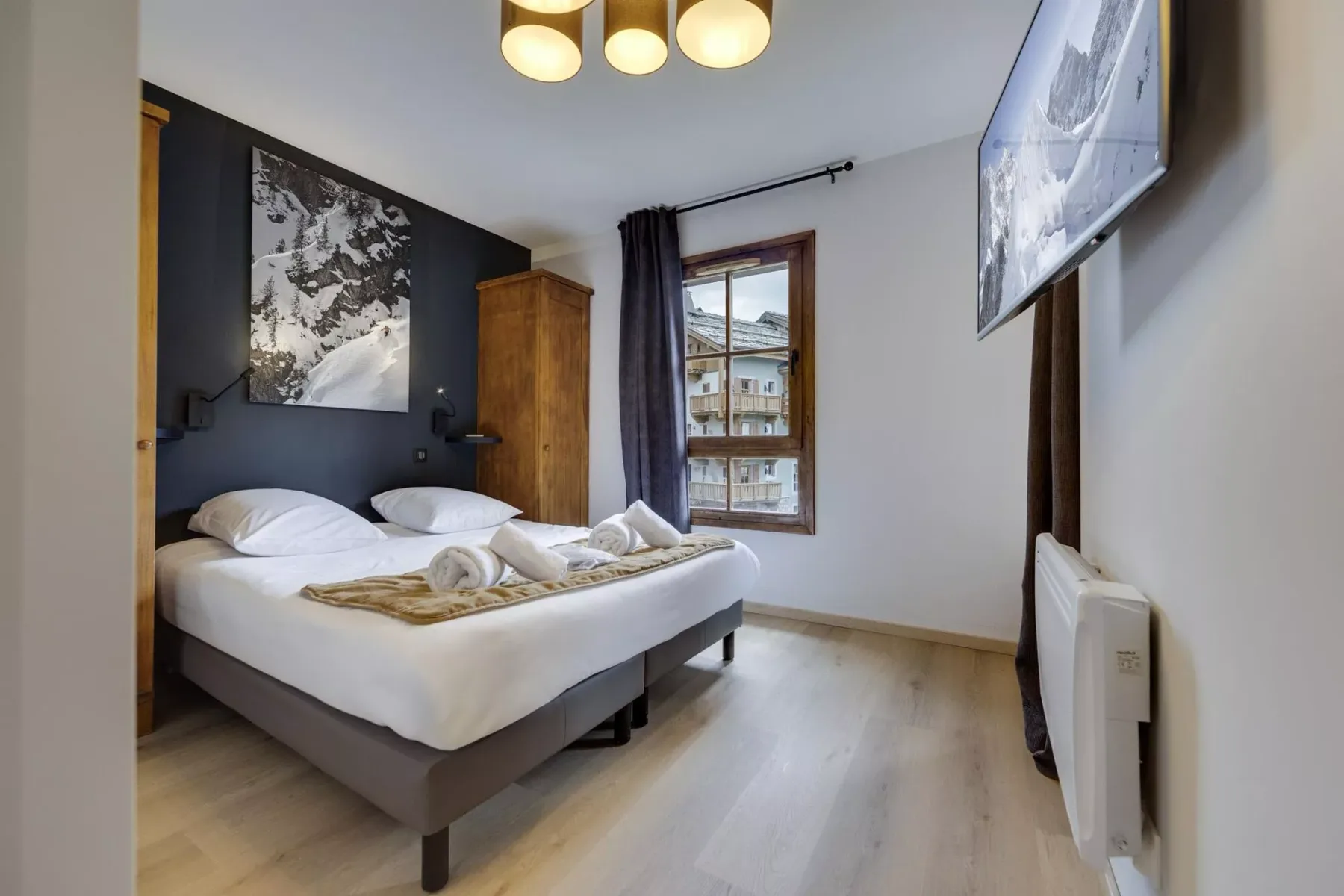 A bedroom with a double bed, a window, and a television mounted on the wall.
