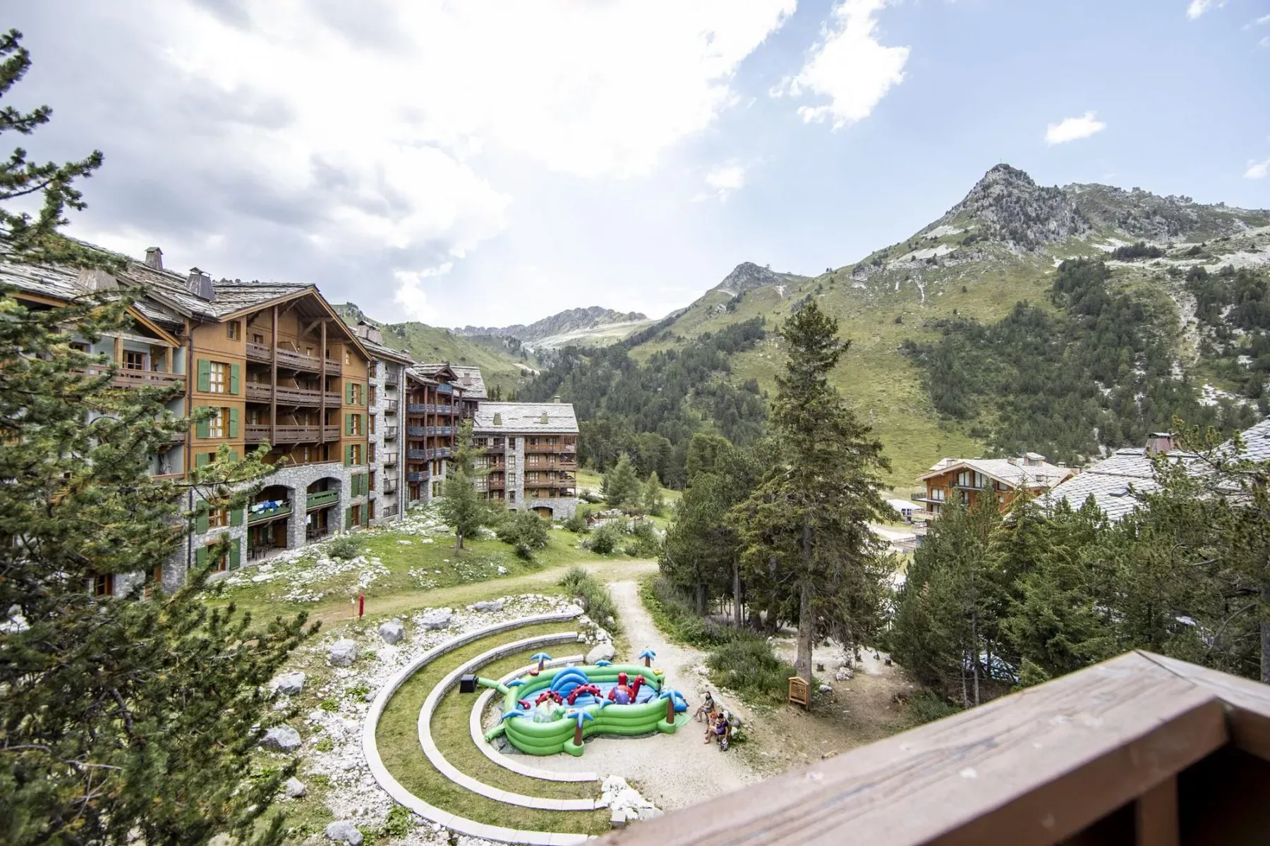 Mountain resort buildings overlook a landscaped courtyard with a small colorful play area.