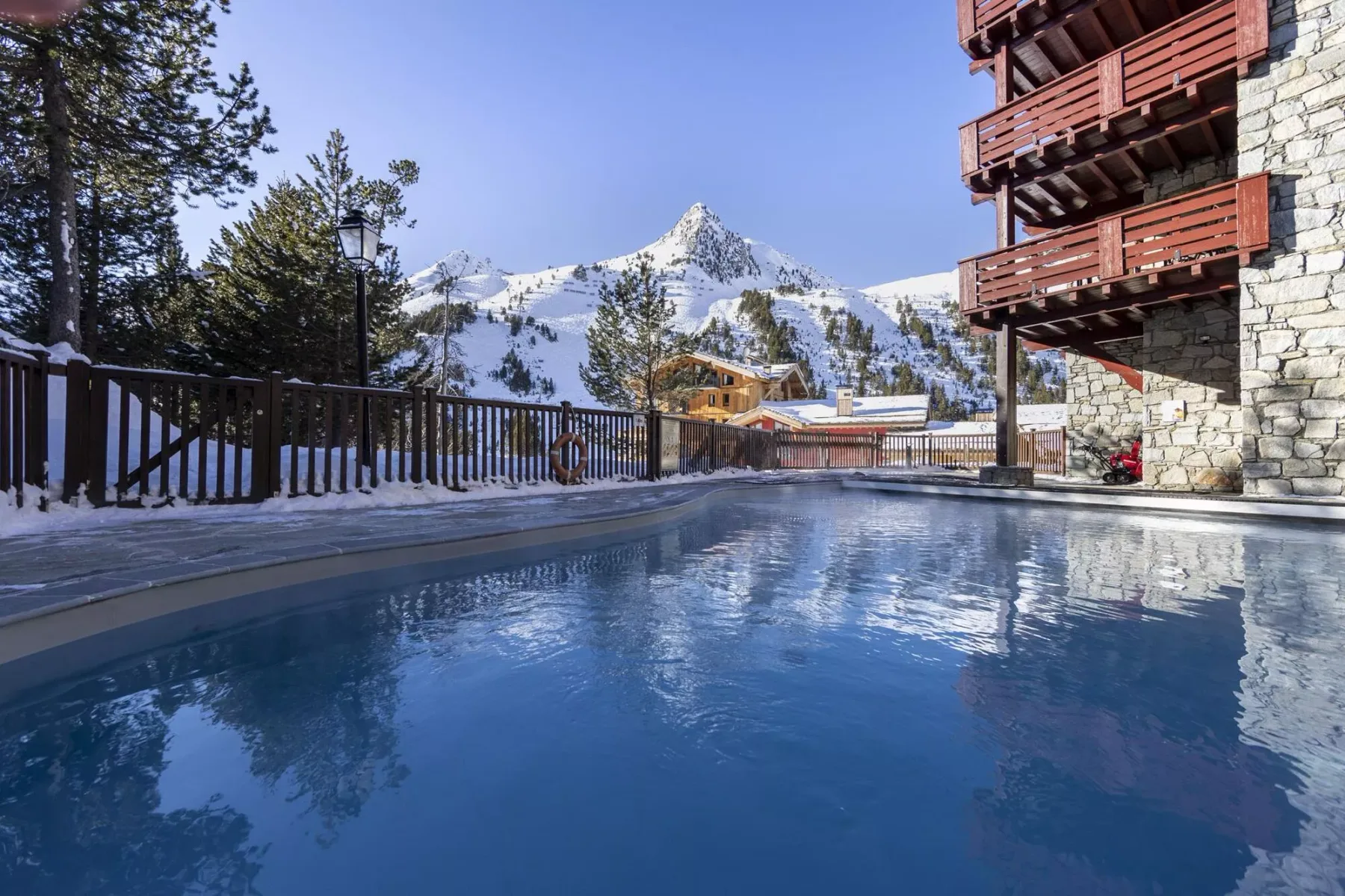 Una vista de montañas nevadas domina una piscina exterior junto a un chalet.