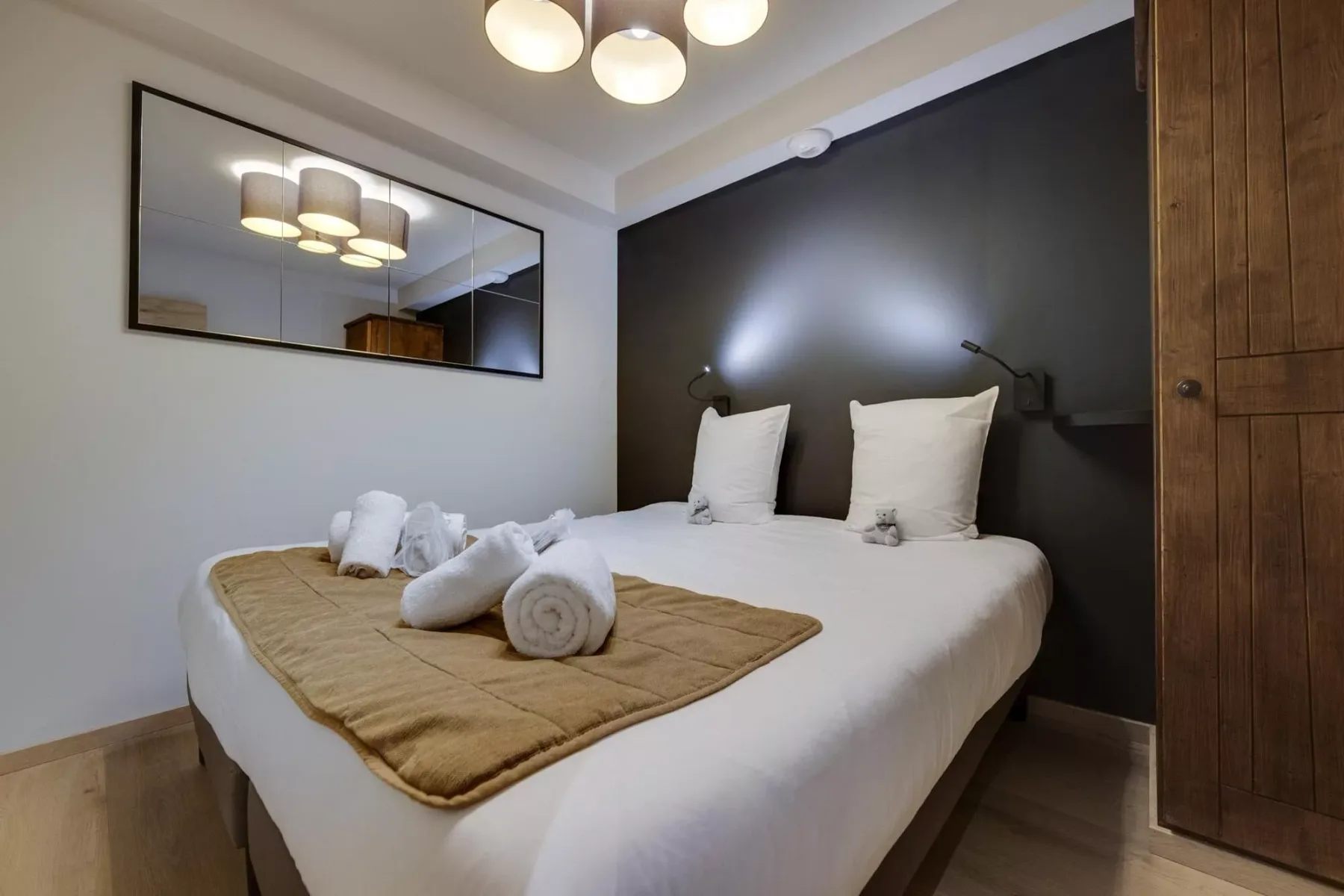 A bedroom with a neatly made bed and a dark accent wall.