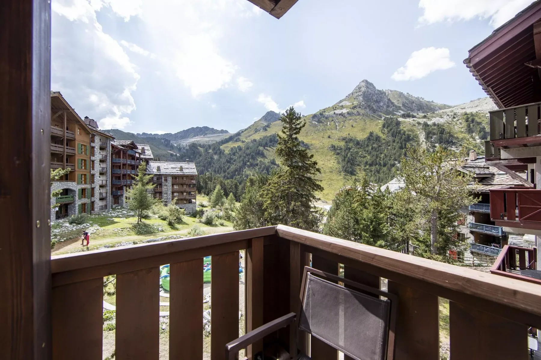 A balcony overlooks mountain slopes, trees, and nearby buildings.