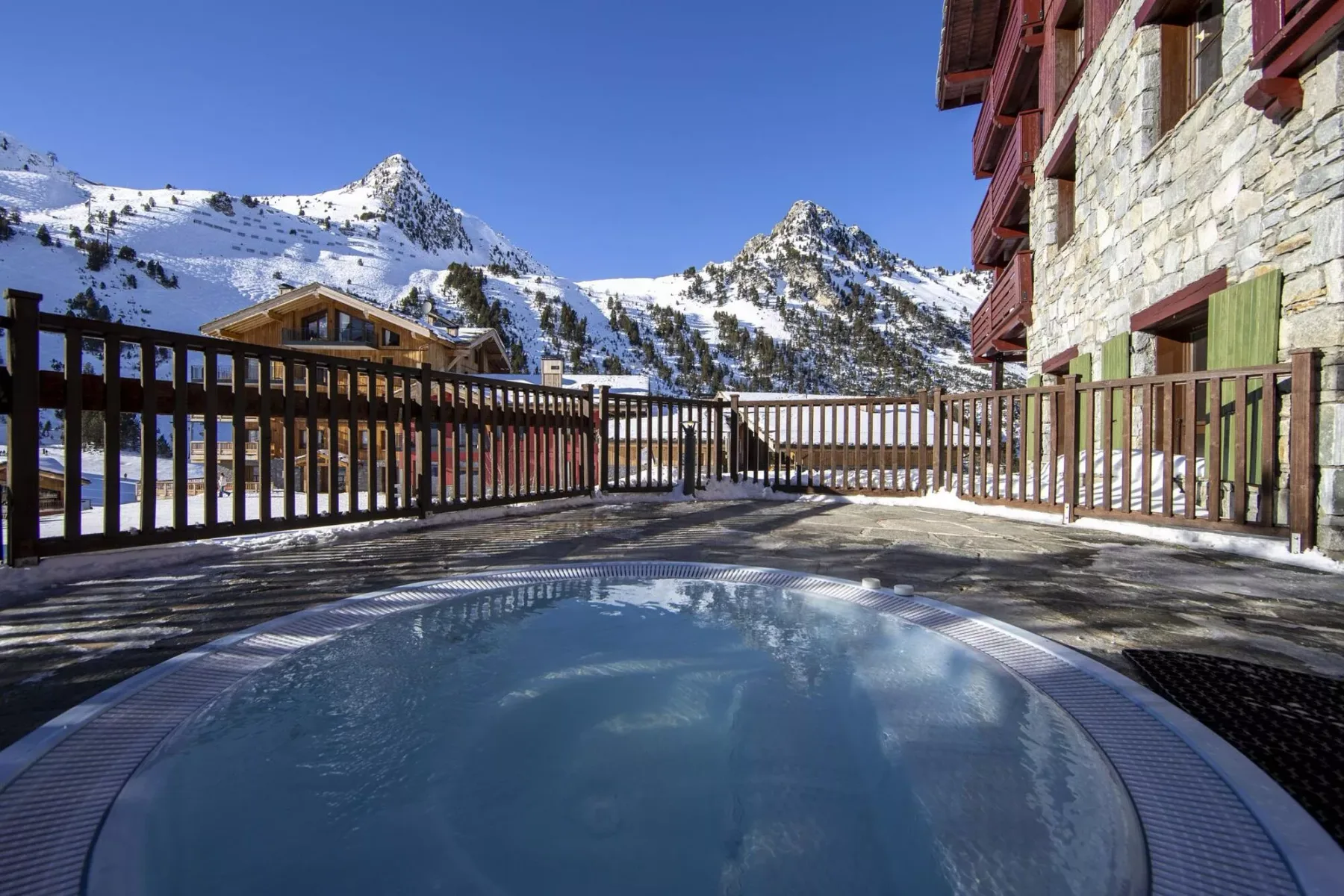 An outdoor pool sits beside a stone building, with snowy mountains in the background.